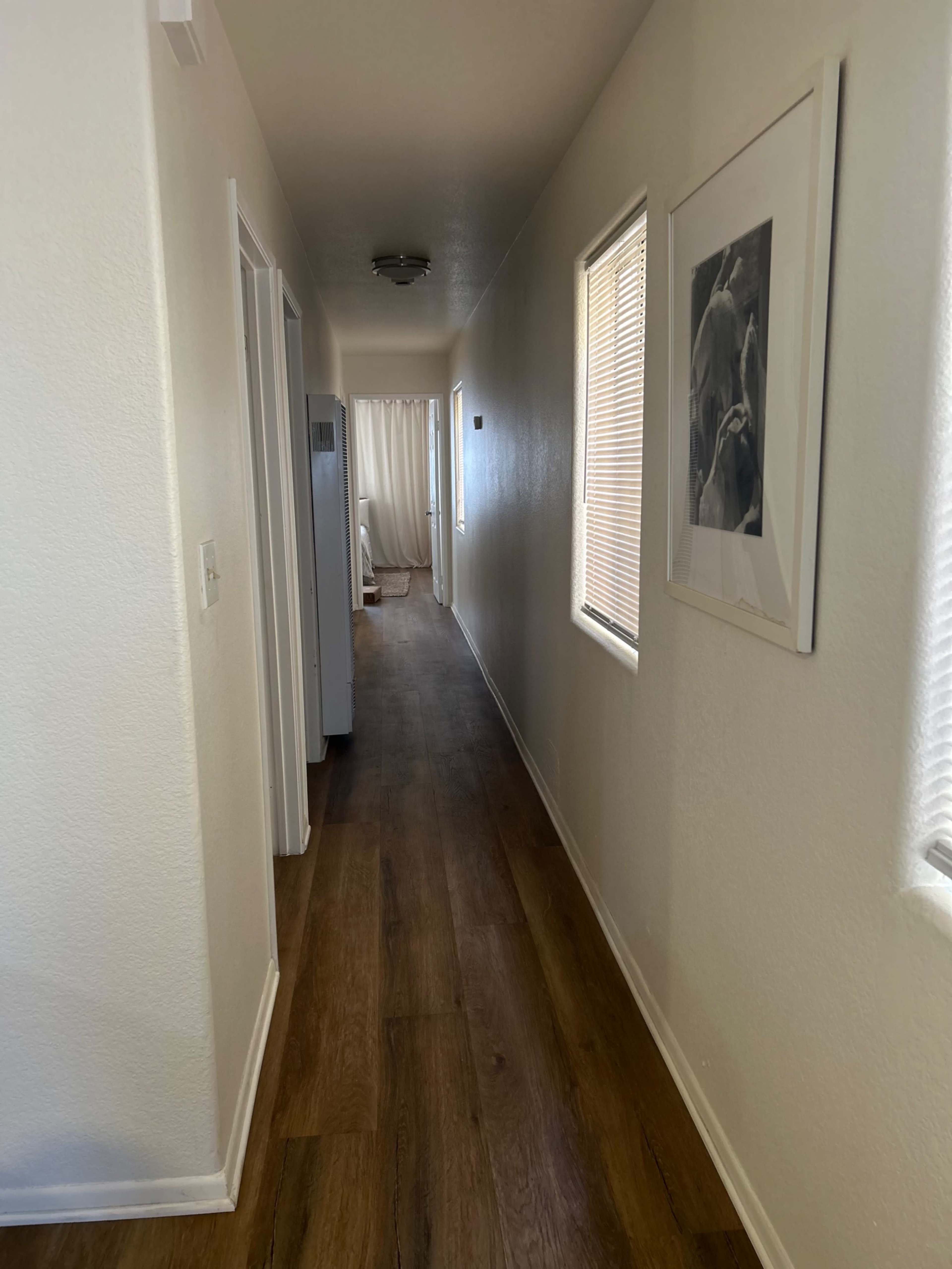 The image shows a narrow hallway with light-colored walls, wooden flooring, and doors leading to adjacent rooms.