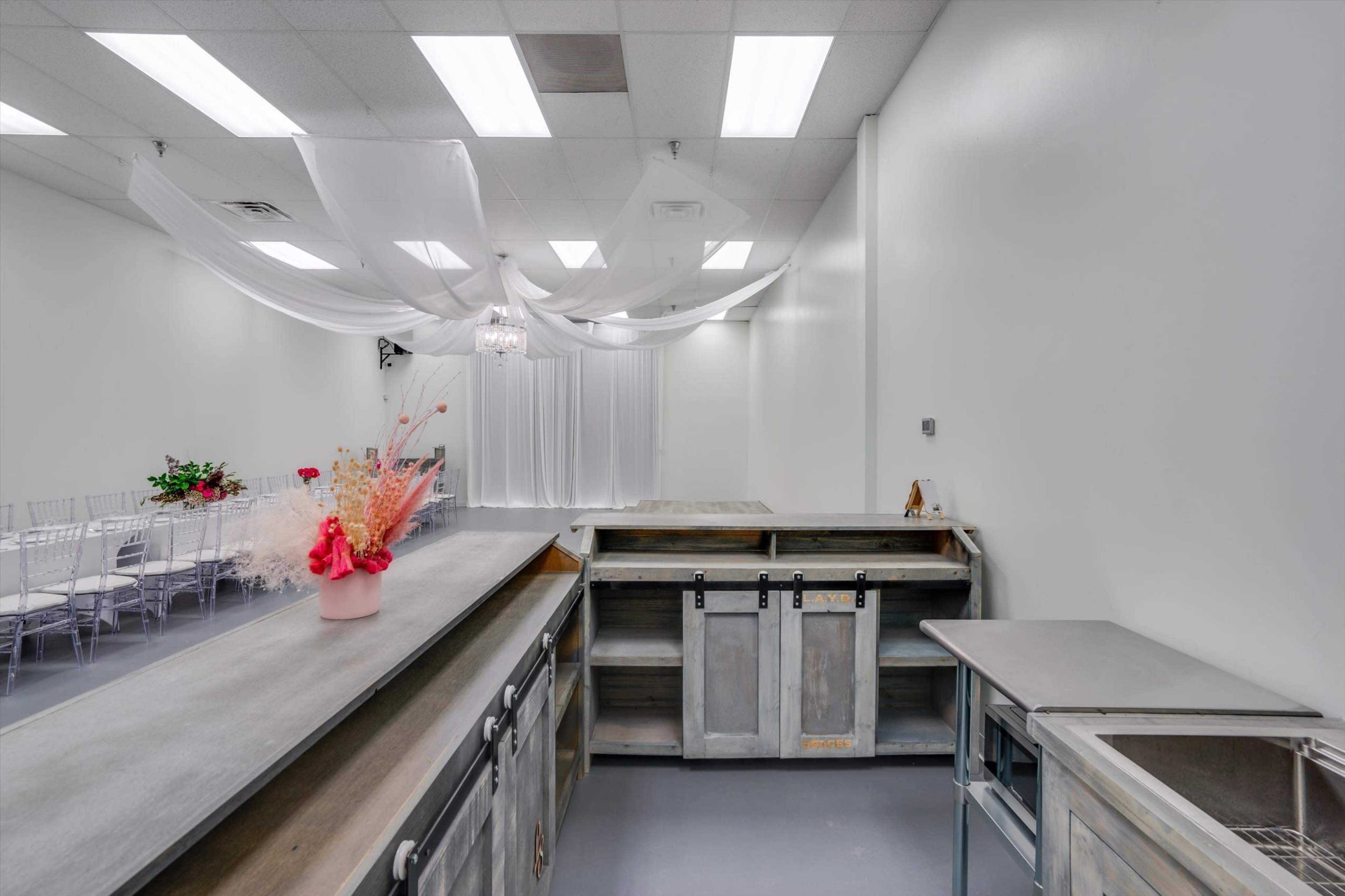 The image shows a spacious reception area with white walls, a decorated table with a small flower arrangement, and a doorway leading to a seating area with chairs and draped fabric overhead.
