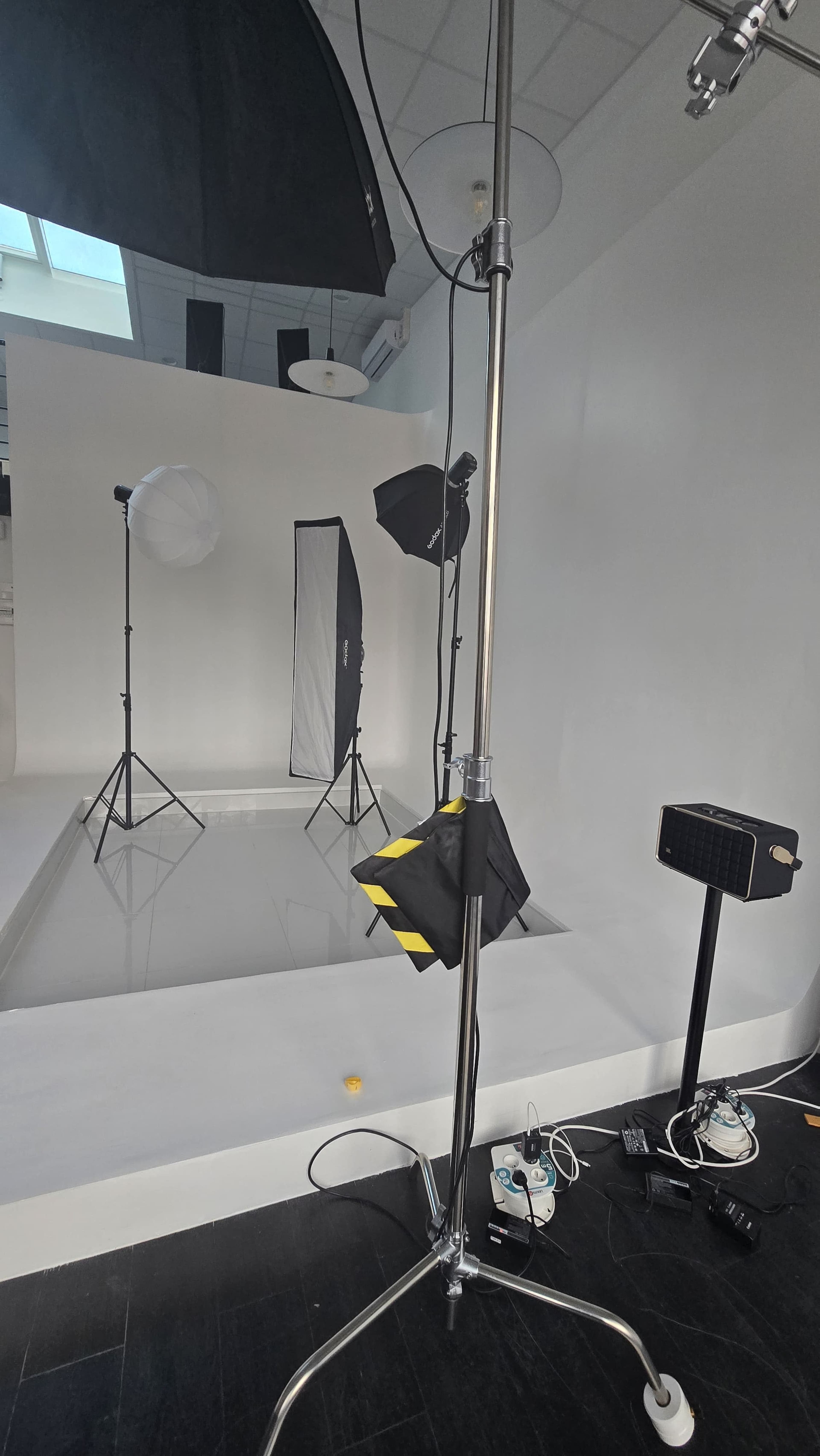 The image shows a photography studio equipped with lighting equipment, including two softboxes, a light stand, and a backdrop, on a clean, white set.
