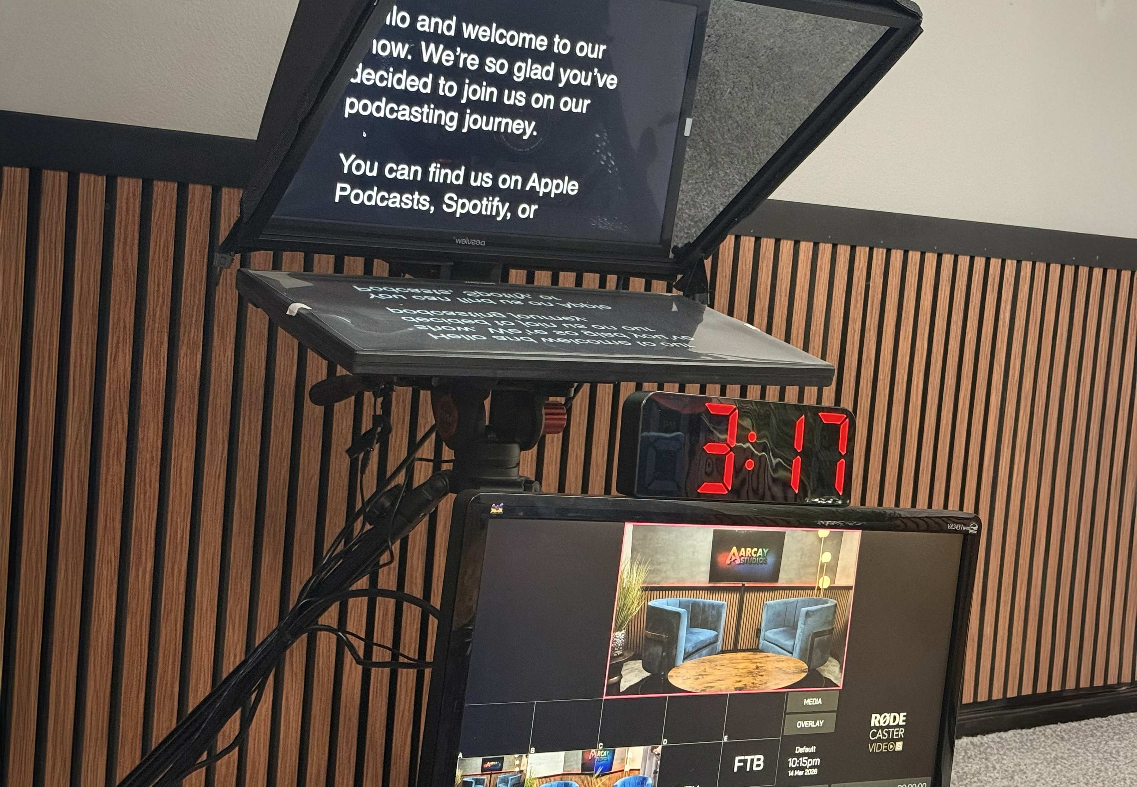 A teleprompter displays a script while a clock shows the time in a studio setting.