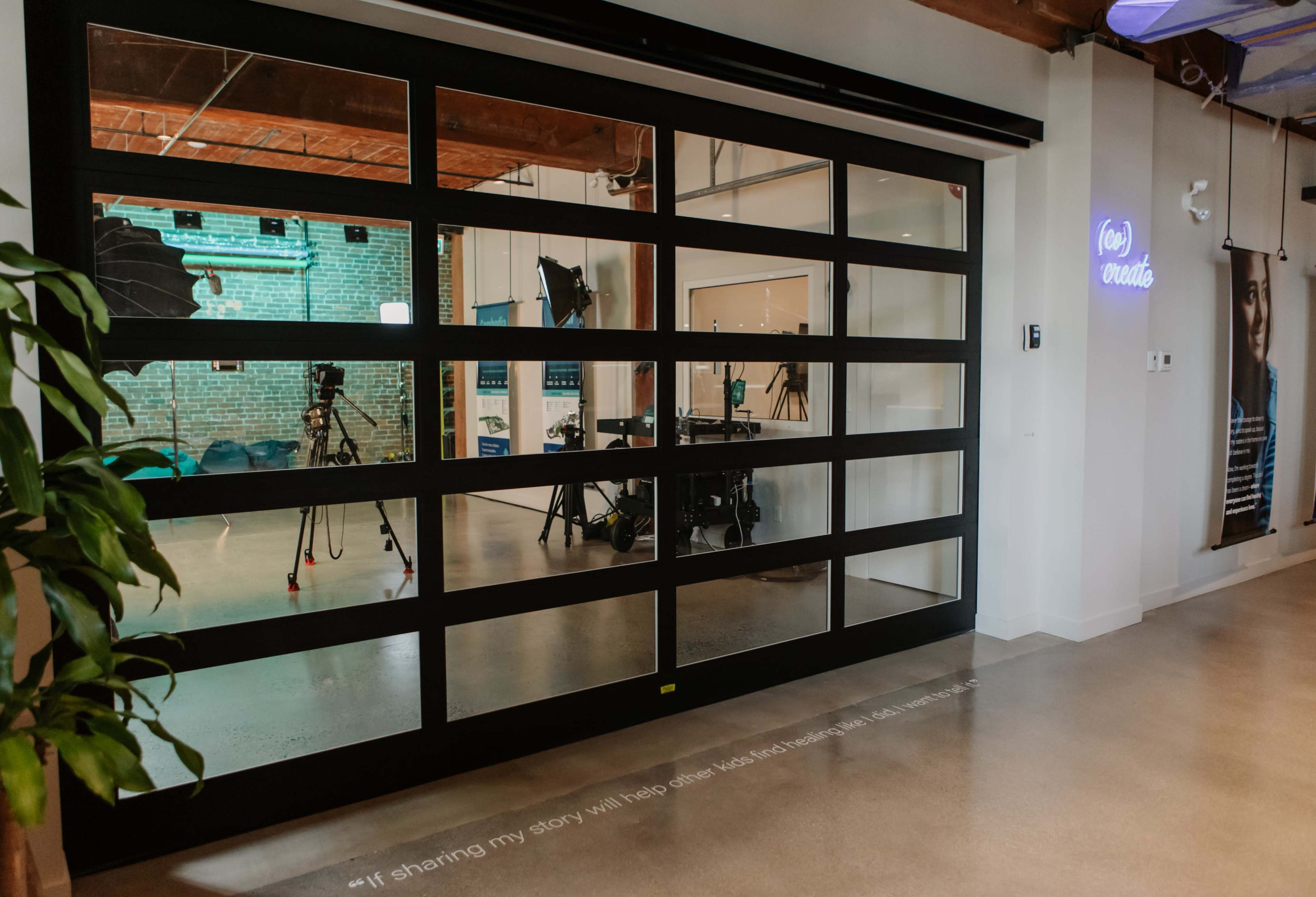 A large glass garage door opens to a studio space with cameras and lighting equipment set up against a brick wall.