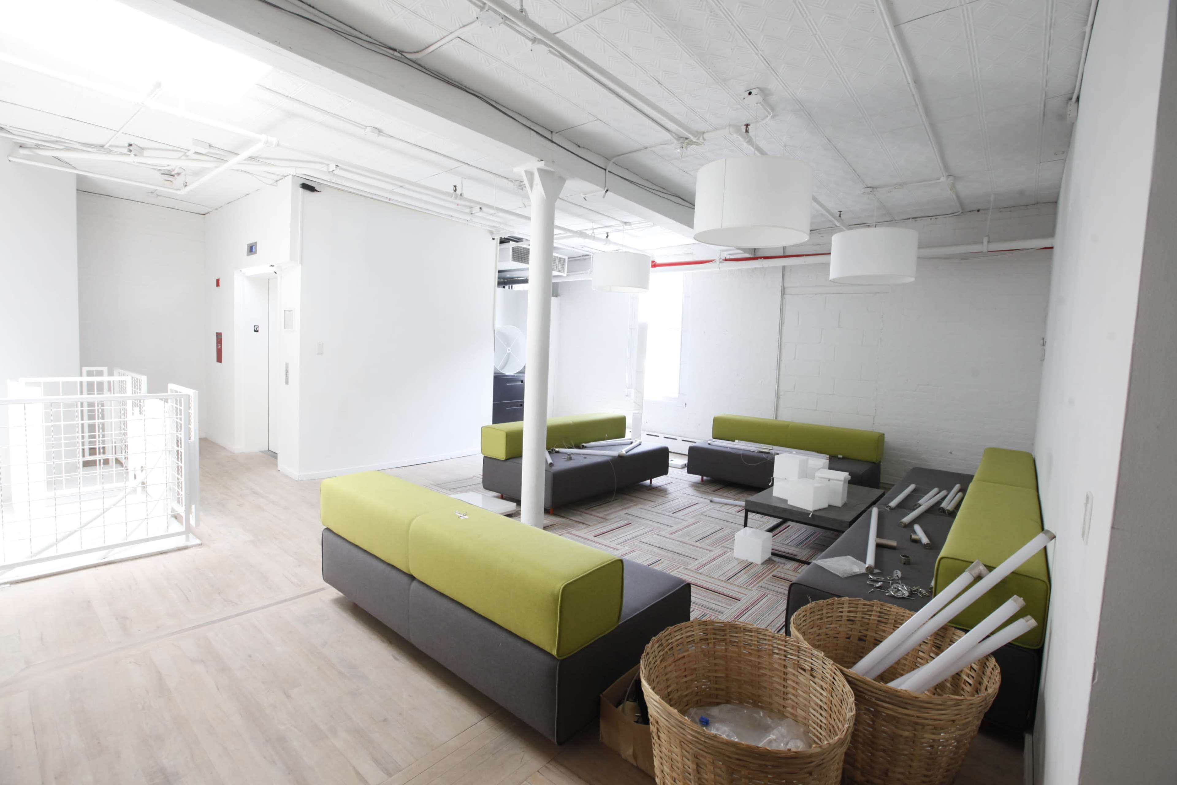 A modern office space featuring green and gray seating arrangements, a light-colored floor, and baskets containing miscellaneous items.