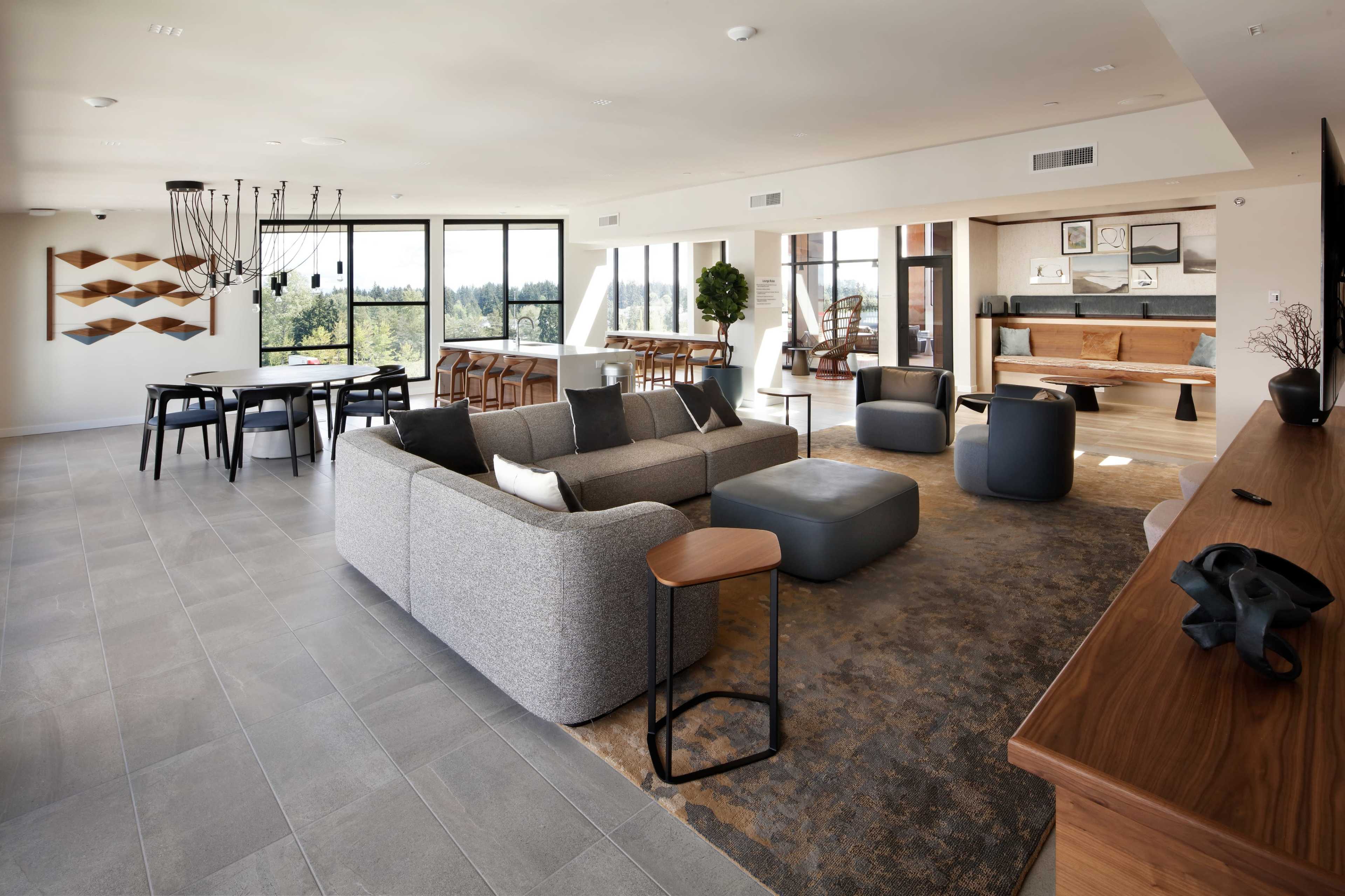 A modern open-concept living space with a gray sofa, a coffee table, and various seating arrangements, featuring large windows that provide natural light.