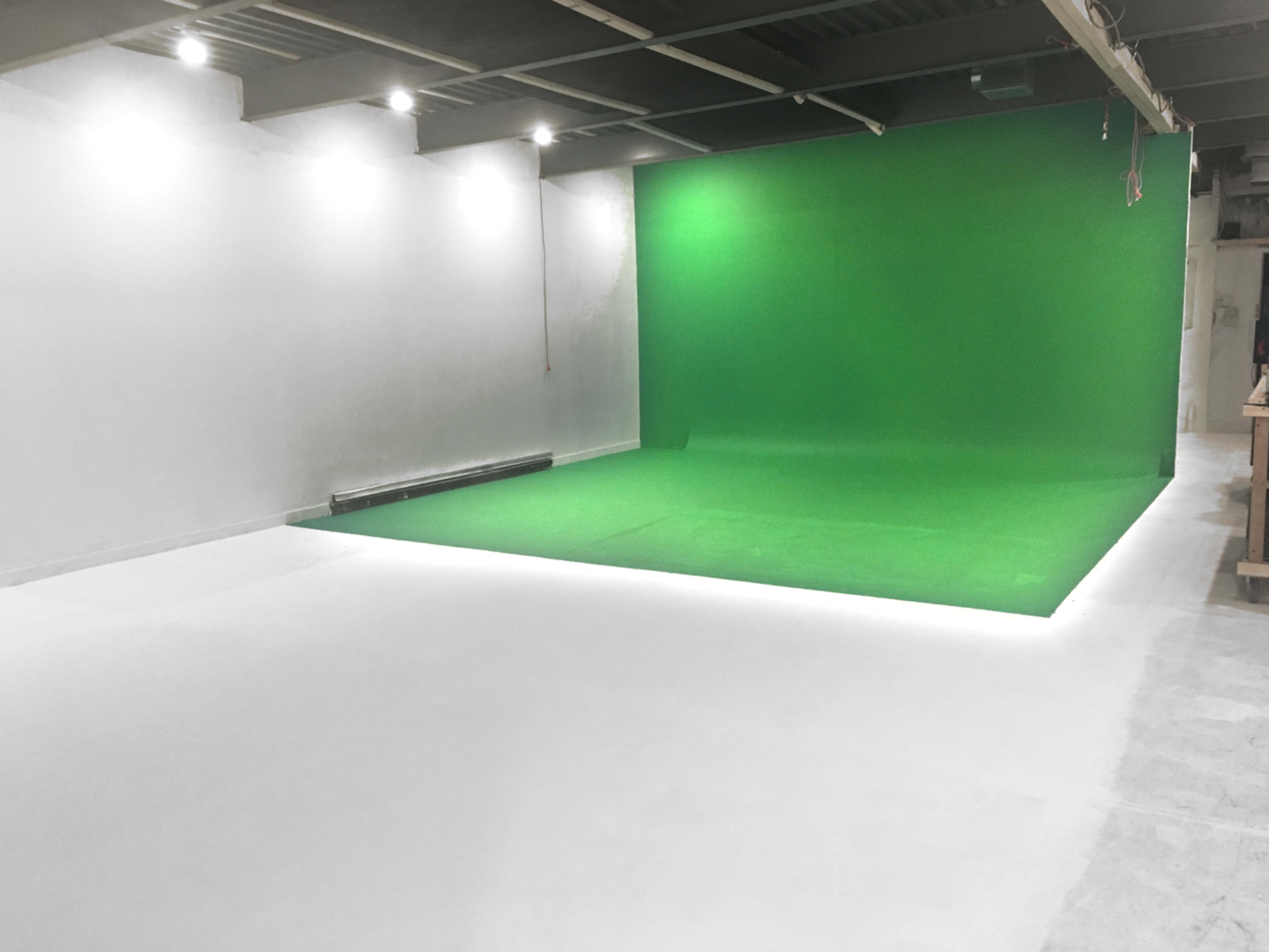 A studio space with a green screen backdrop on one side and a white floor.