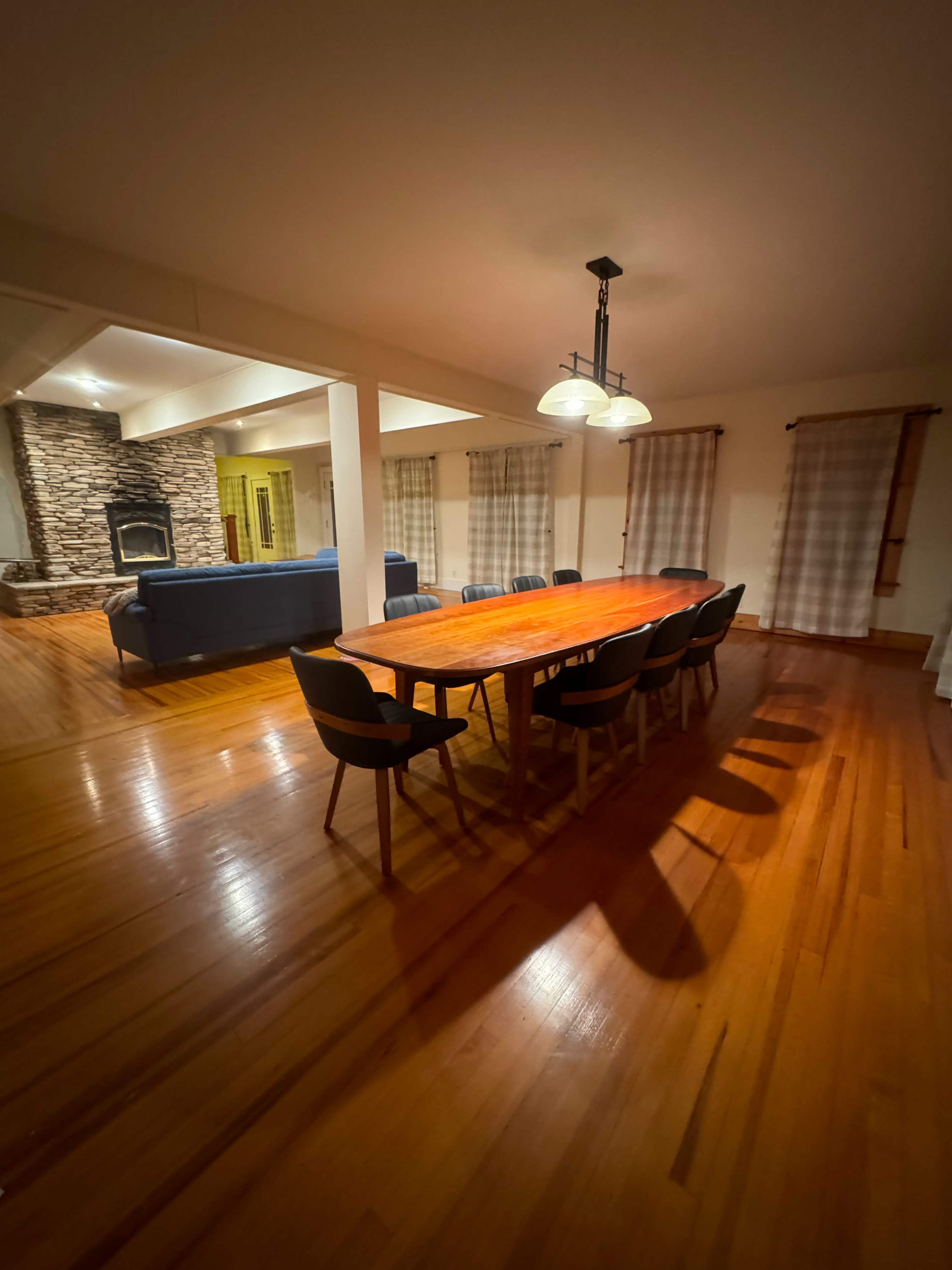 A dining area with a long wooden table and chairs, adjacent to a living space featuring a stone fireplace and a sofa.