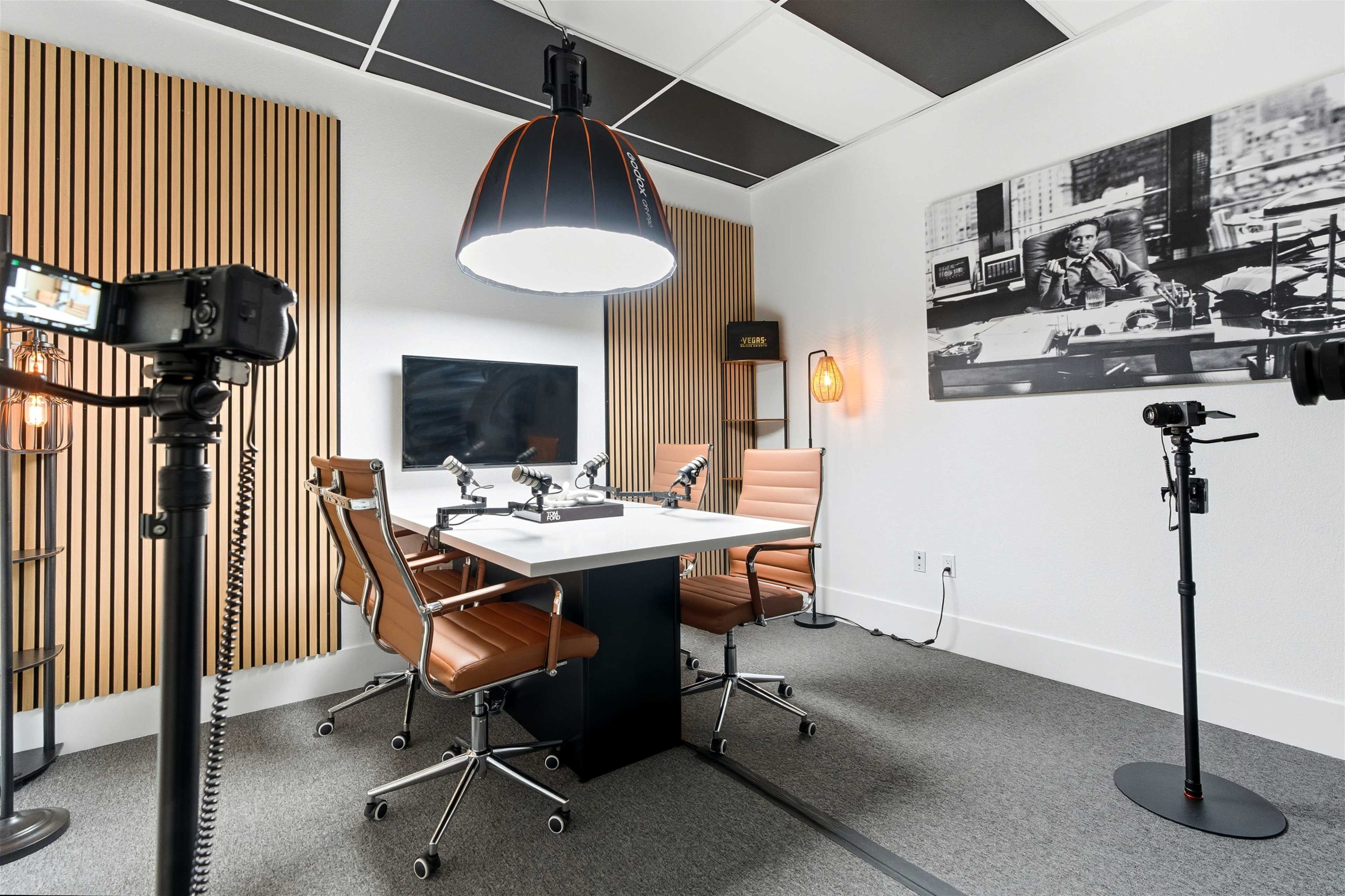 The image shows a modern conference room with a white table, four leather chairs, a large pendant light, and a black and white photo on the wall.