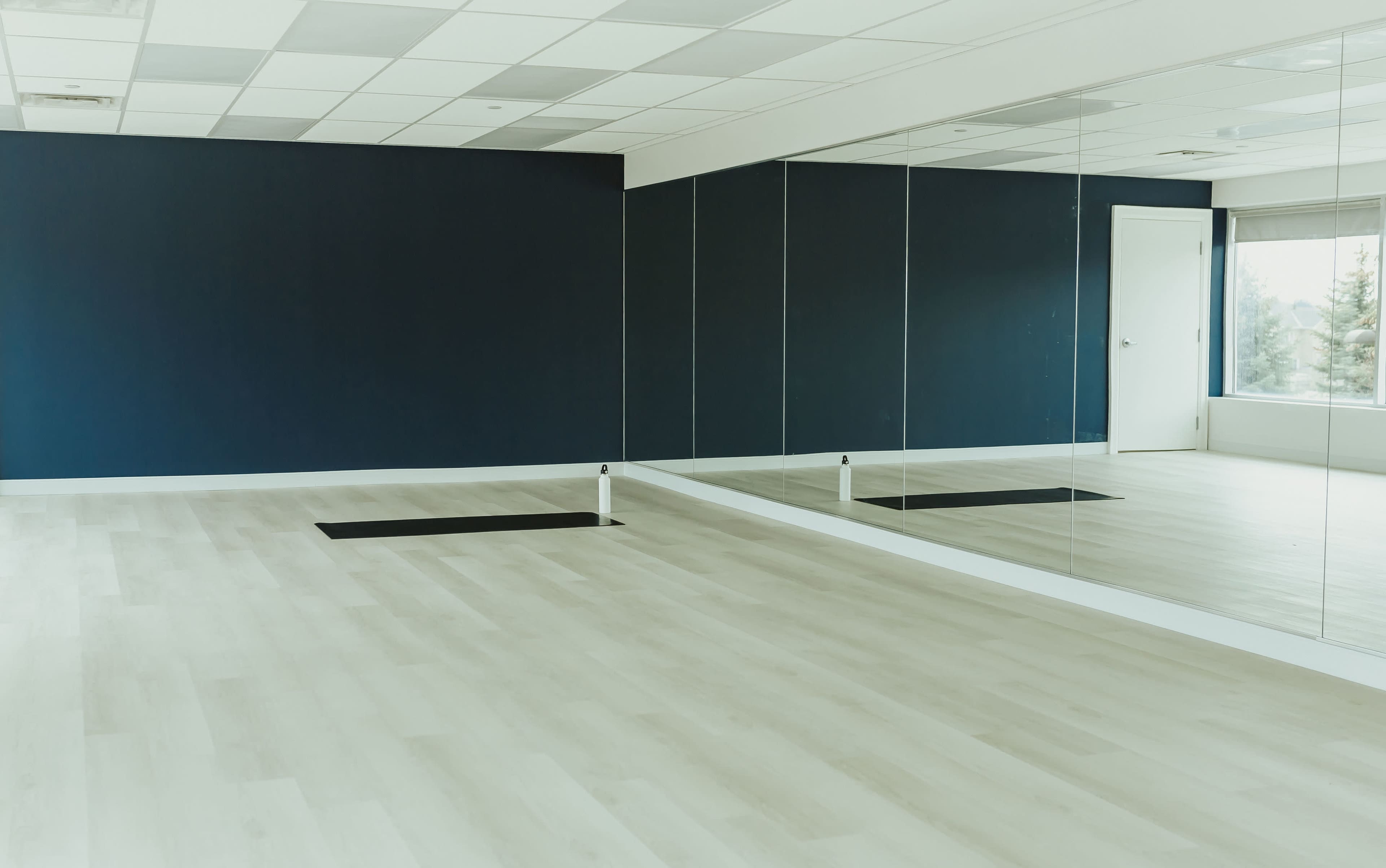 An empty room with light-colored wooden flooring, a dark blue wall, and a large mirror on one side.