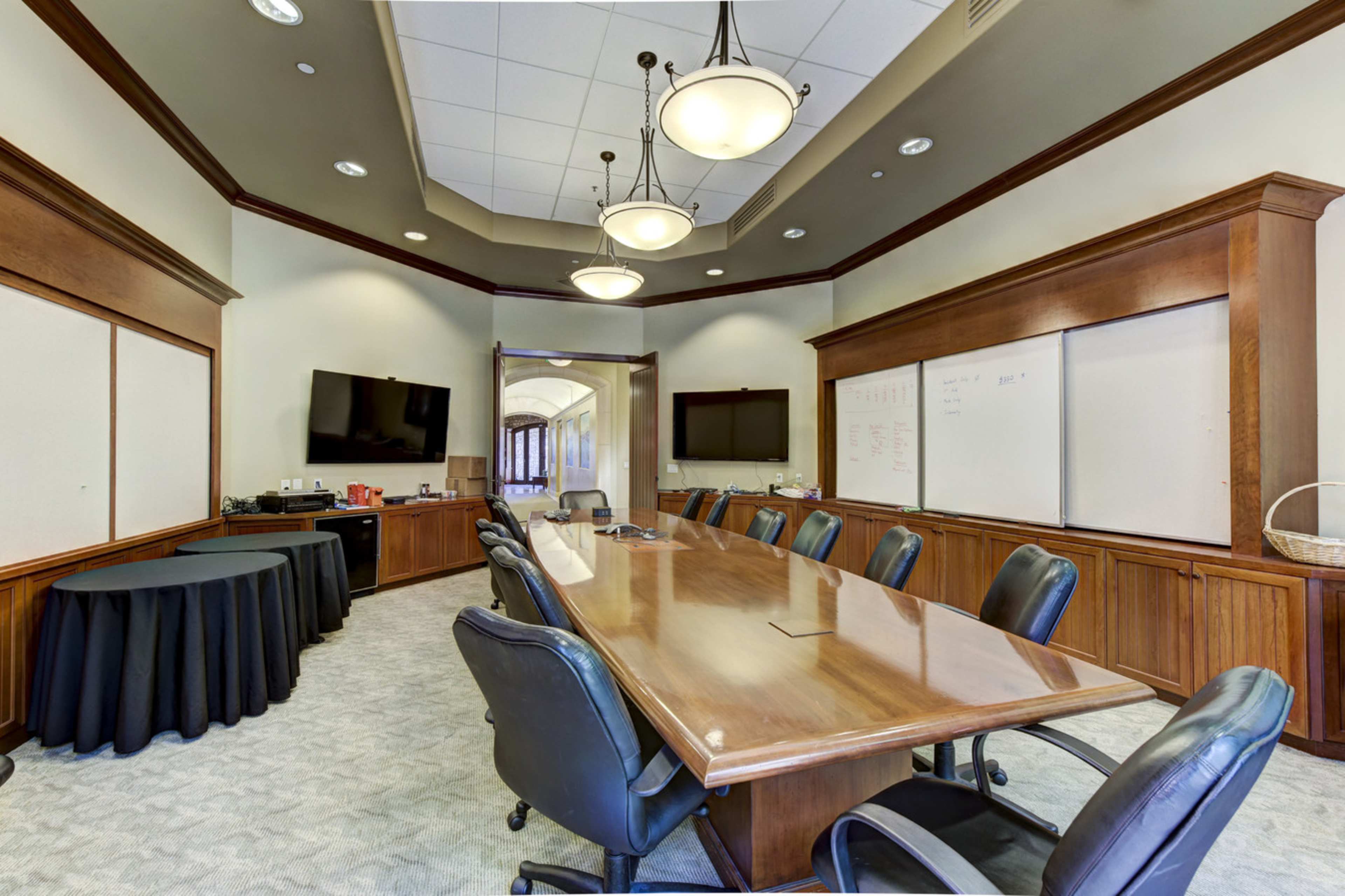 A large conference room with a long wooden table surrounded by black chairs and two flat-screen TVs mounted on the walls.
