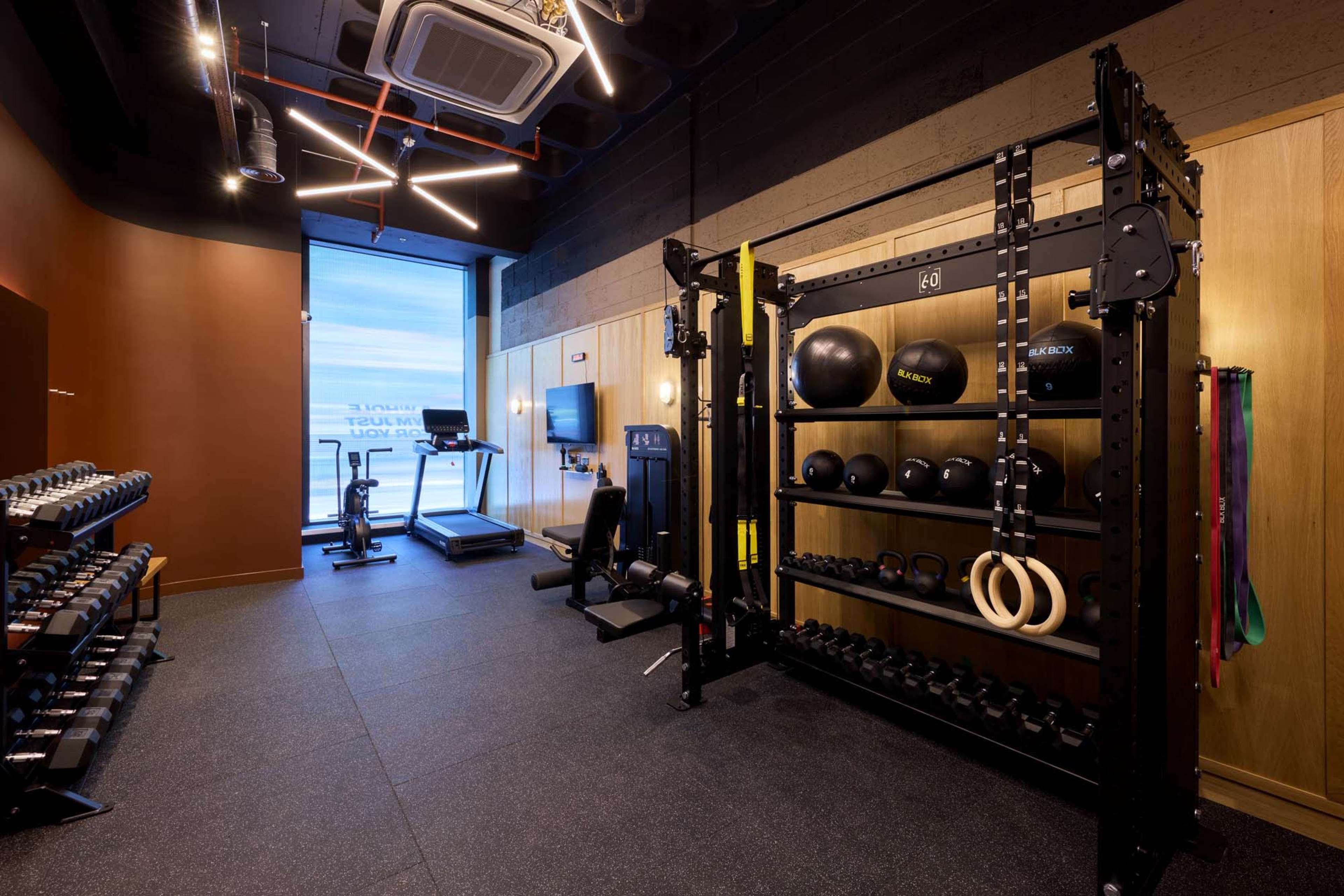 The image shows a modern gym with various exercise equipment, including dumbbells, a power rack, and a treadmill, arranged neatly in a well-lit space.