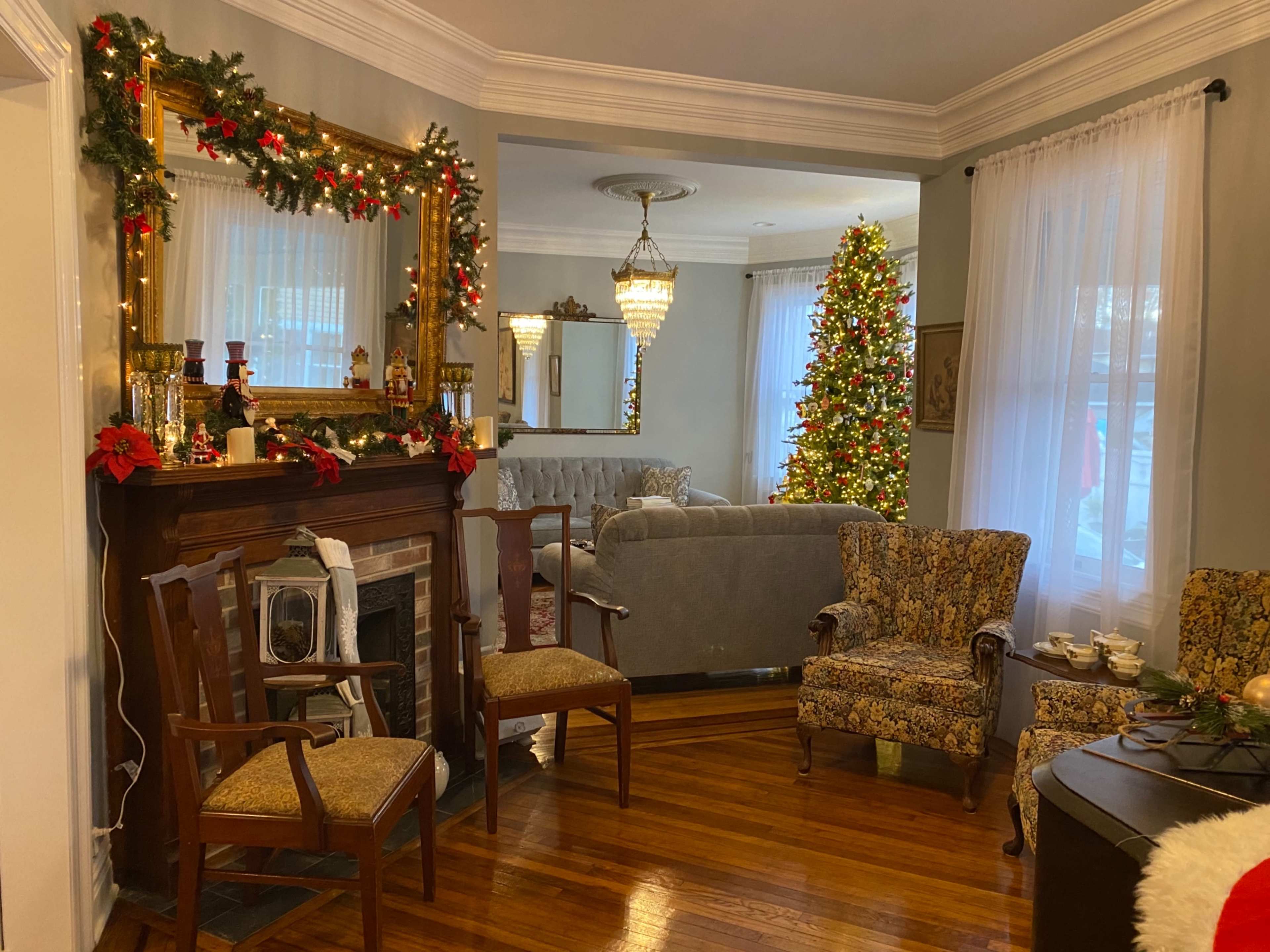 A living room decorated for the holidays features a Christmas tree, garlands on the mantel, and traditional furnishings.