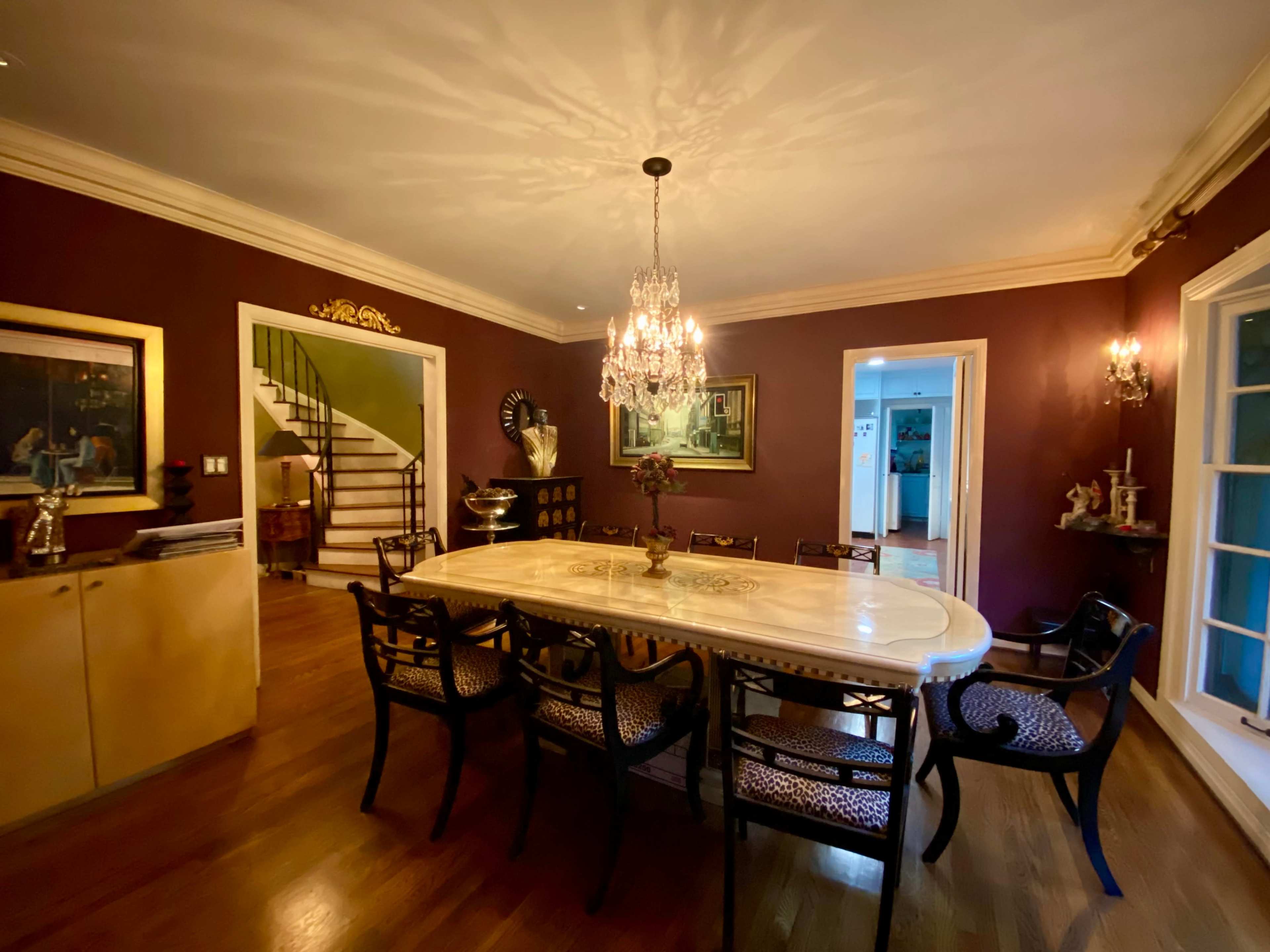 A formal dining room featuring a large table surrounded by ornate chairs, a chandelier overhead, and decorative artwork on the walls.