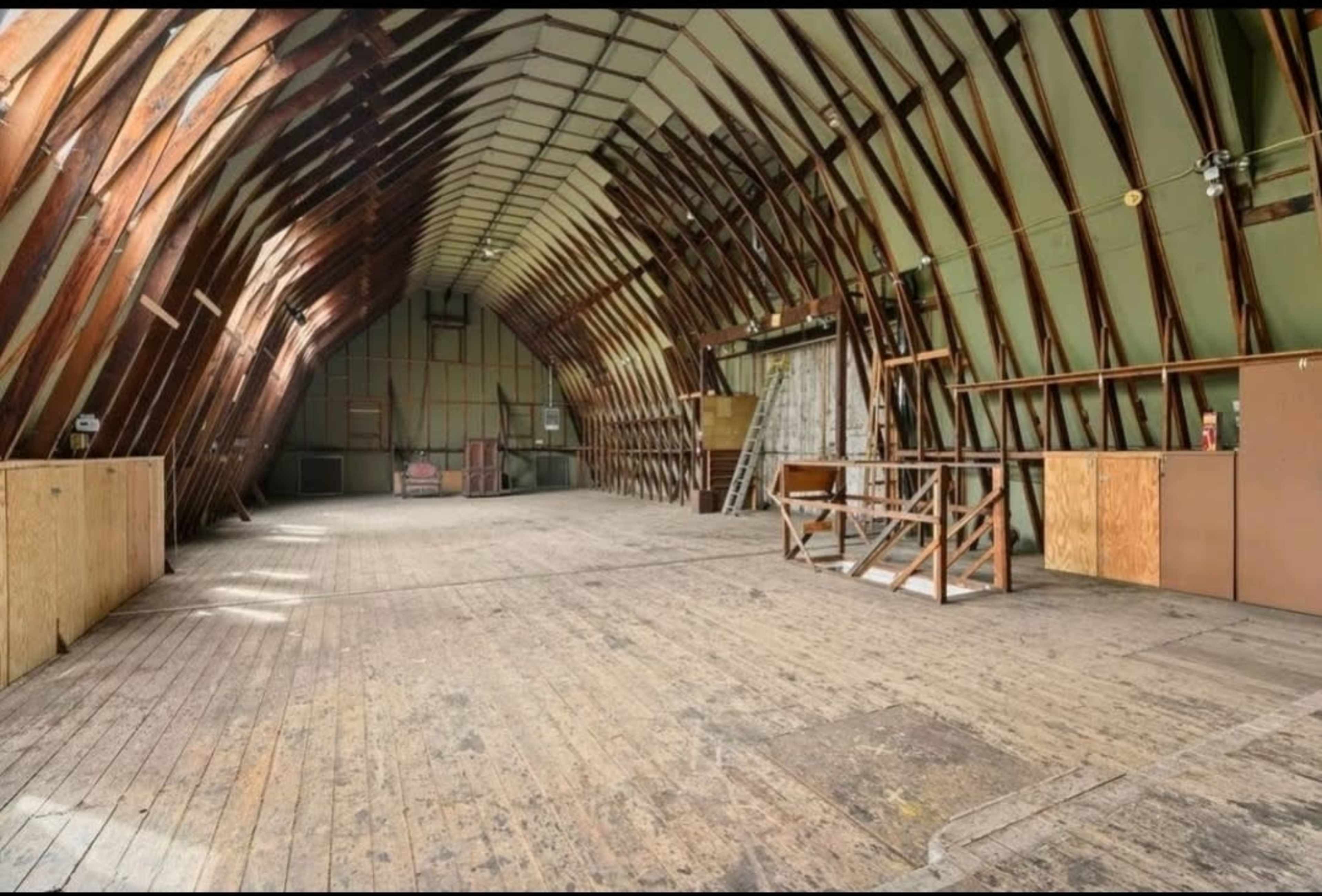 A large, empty barn-like structure with wooden beams and a wooden floor.