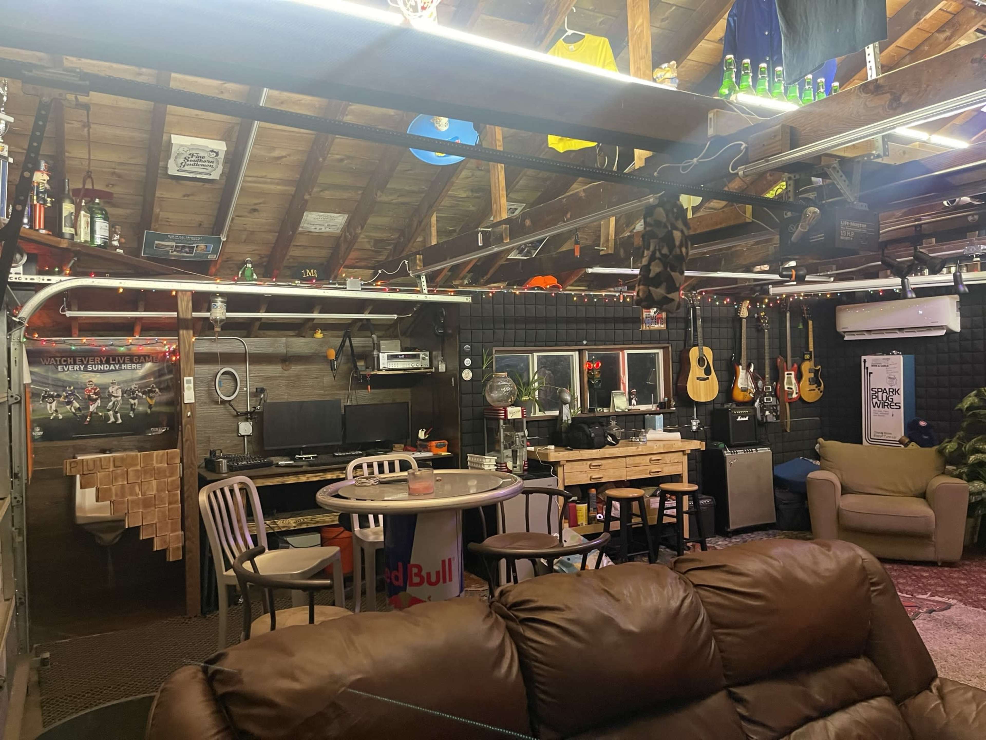 A garage space converted into a recreational area with a seating area, a computer setup, musical instruments, and decorative items hanging from the ceiling.