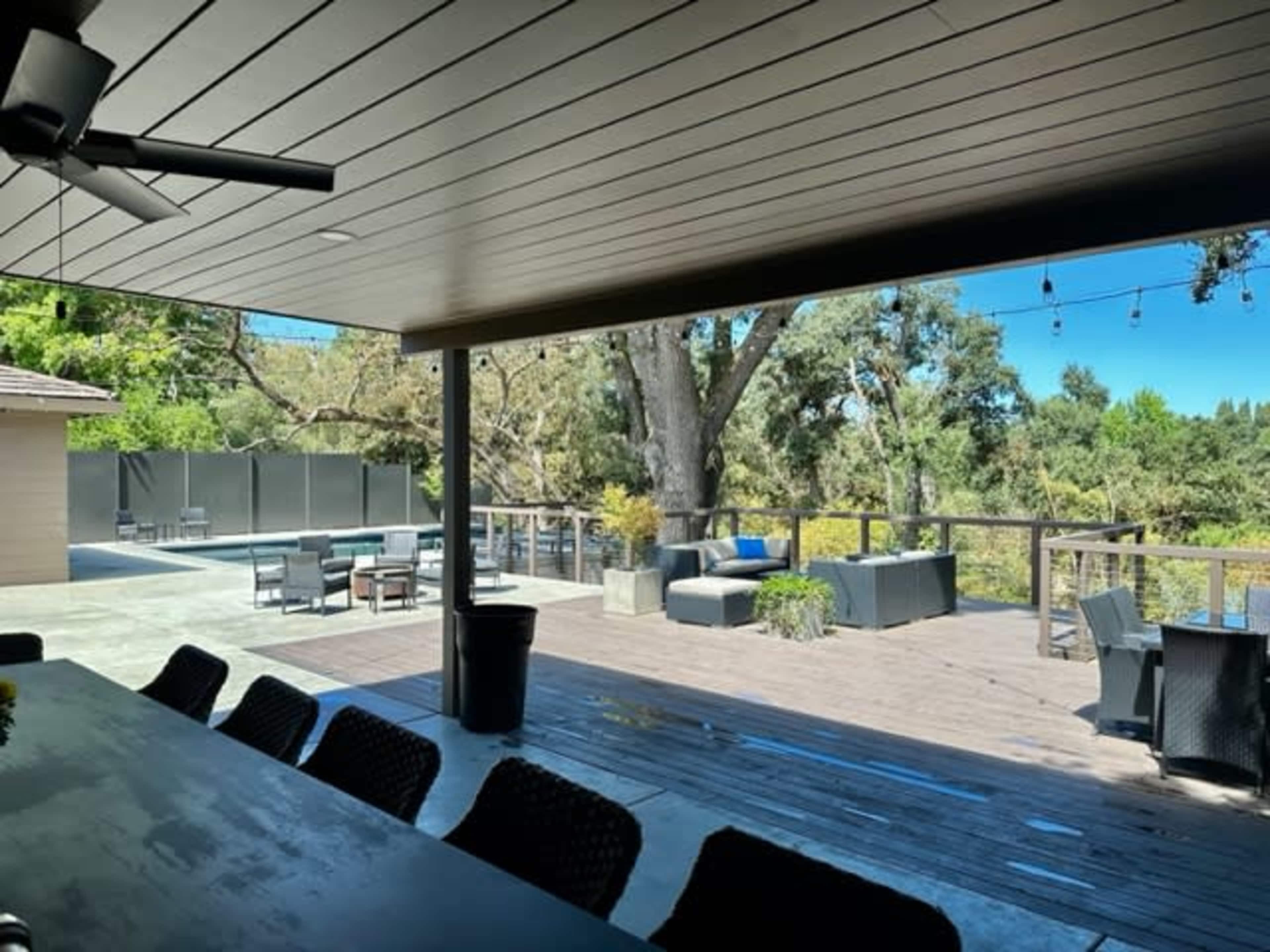 A spacious outdoor deck features seating areas and a dining table, surrounded by trees and a fence.