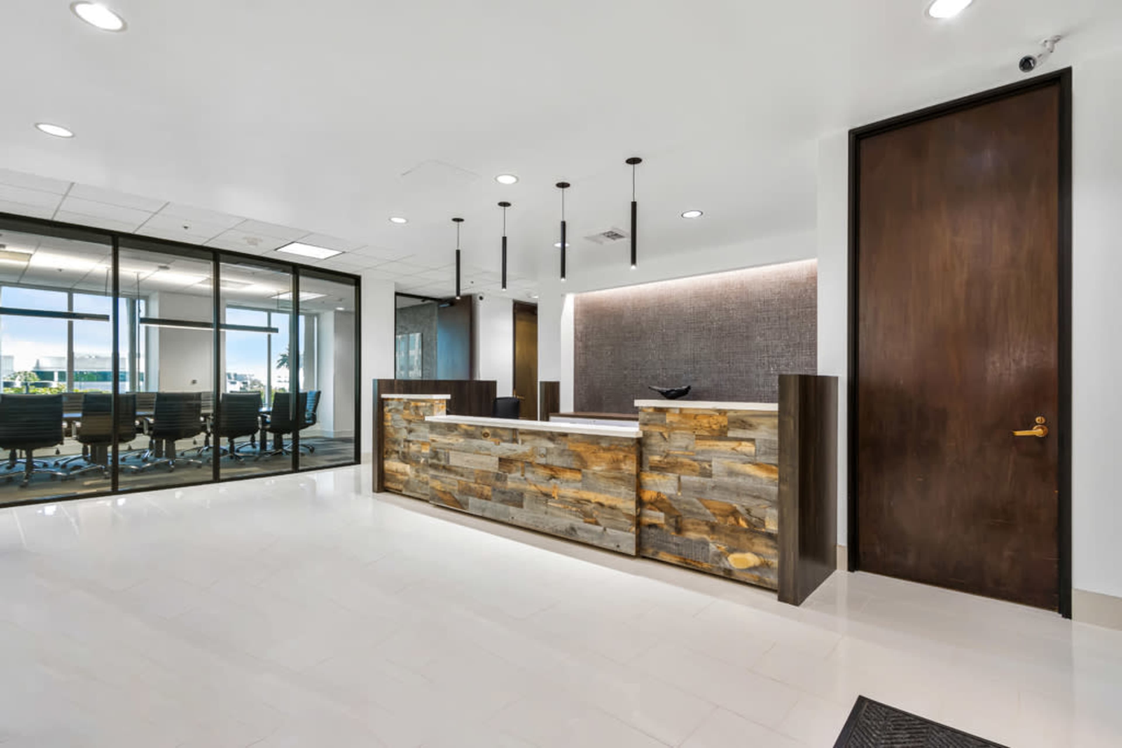 A modern reception area features a stone-clad front desk, large windows overlooking a conference room, and a dark wood door.
