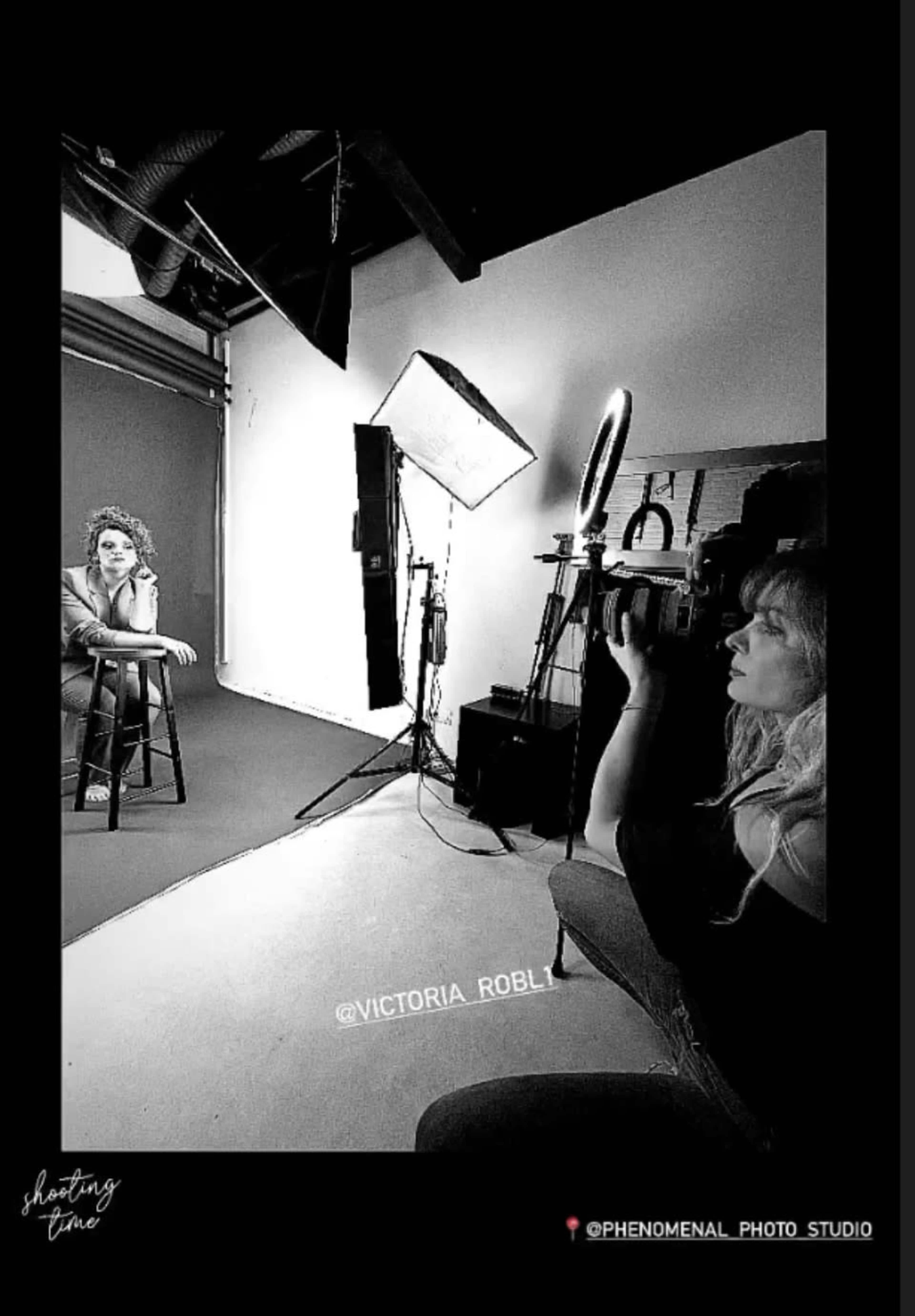 A photographer captures a seated model in a studio, with lighting equipment set up around them.