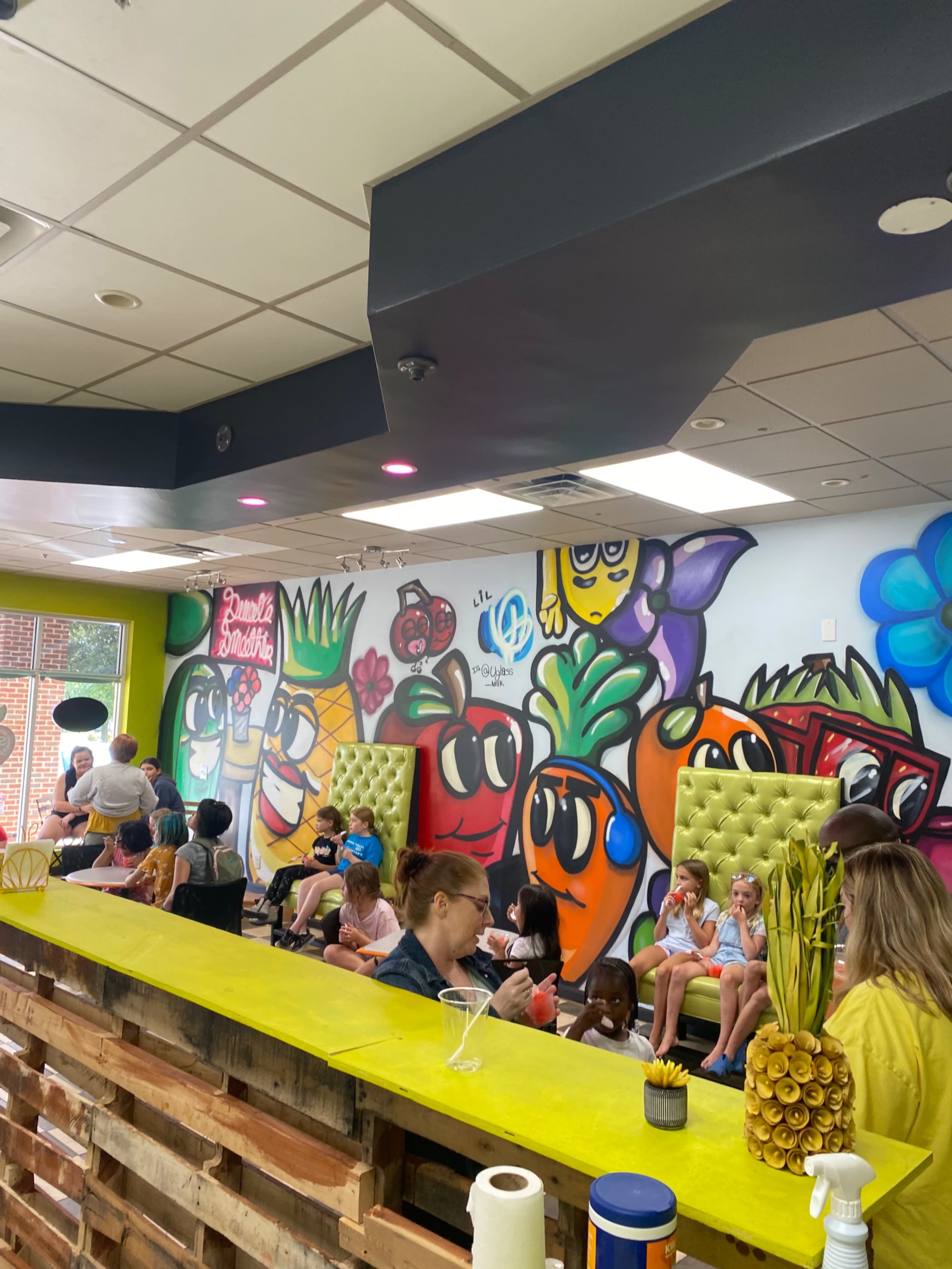 A vibrant café interior with colorful fruit-themed murals, seating areas, and customers enjoying their time.