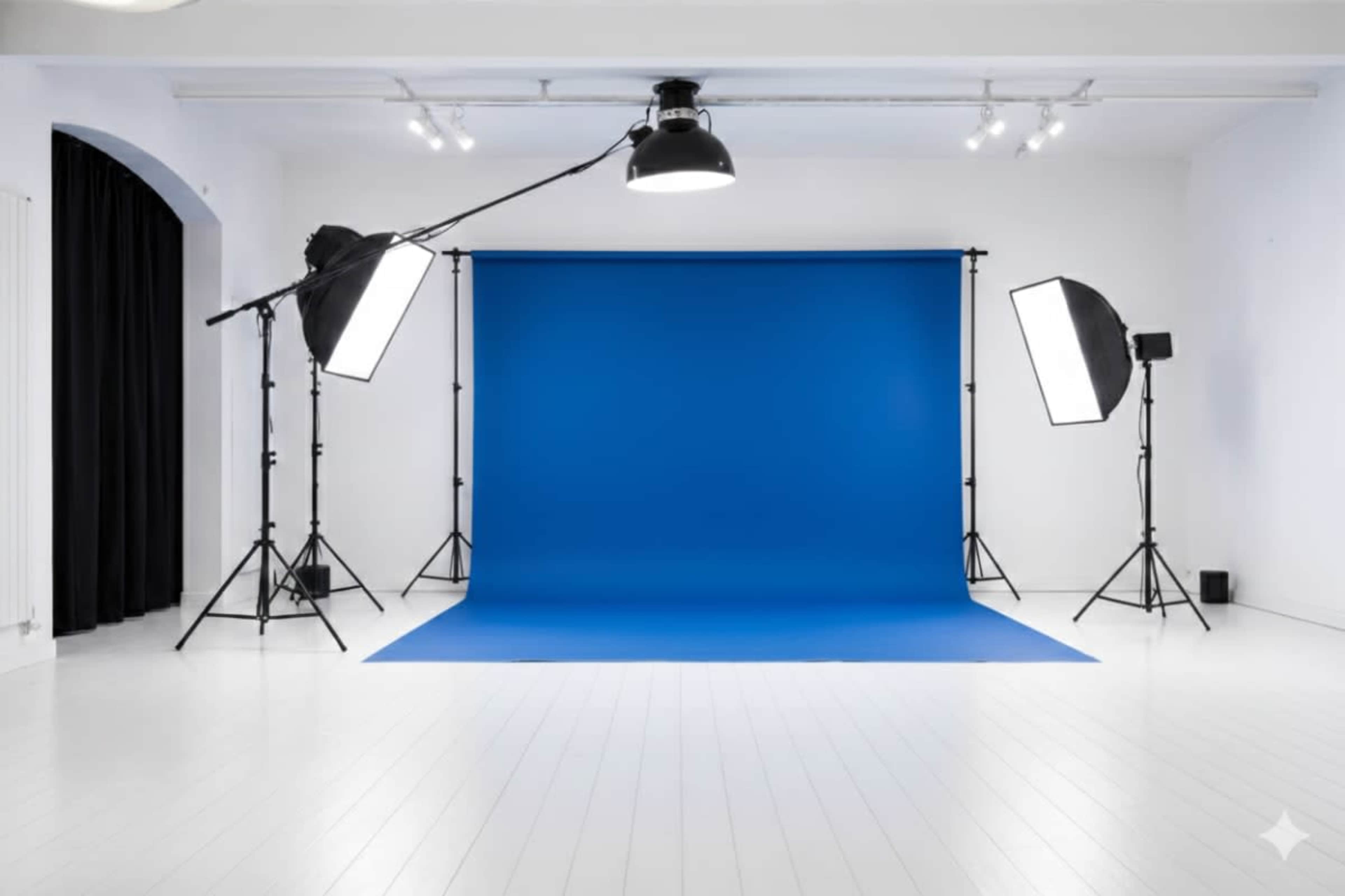 A photography studio features a blue backdrop with two large softbox lights and overhead lighting in a bright, minimalist space.