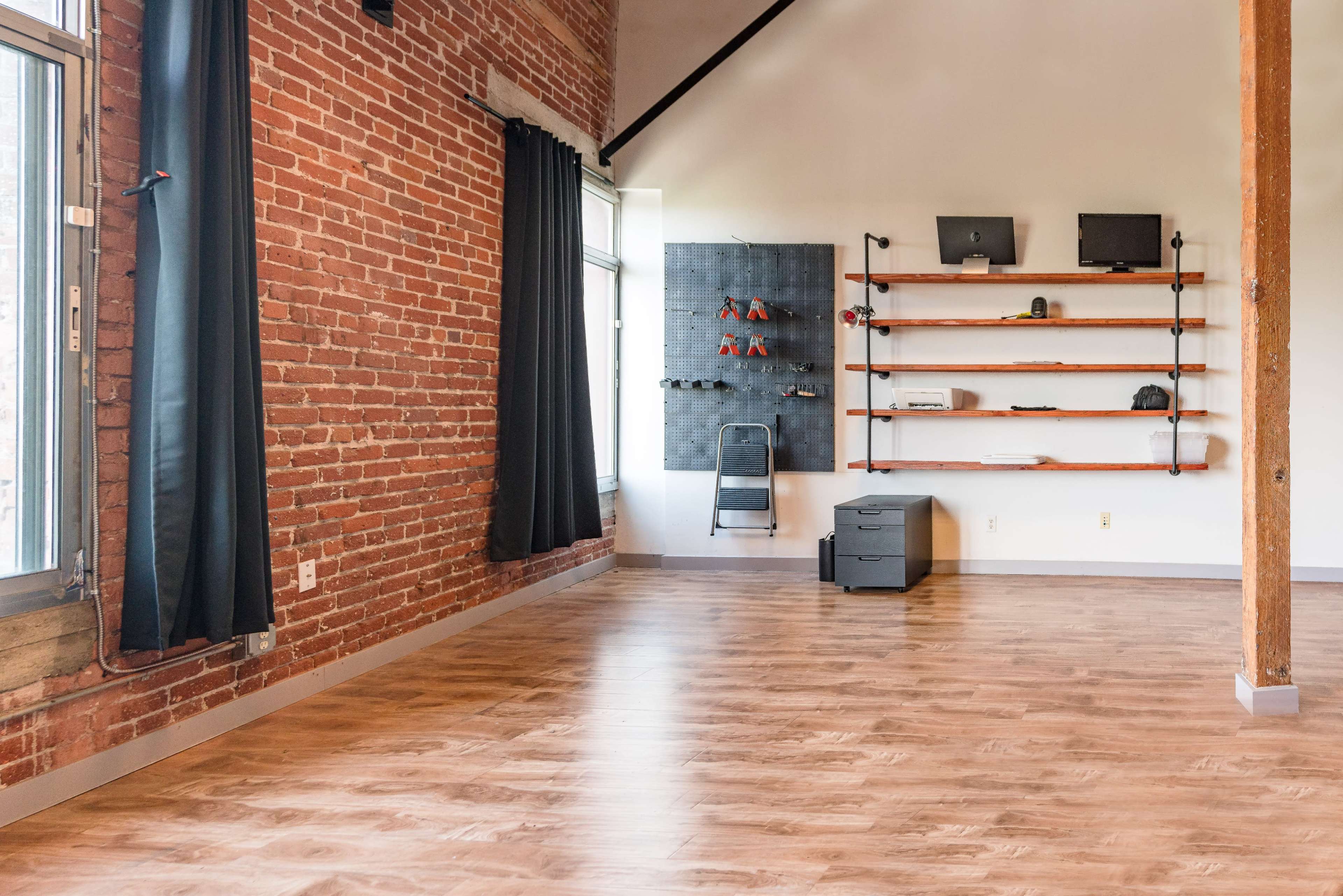 A spacious room with exposed brick walls, polished wooden flooring, and shelves displaying various tools and accessories.