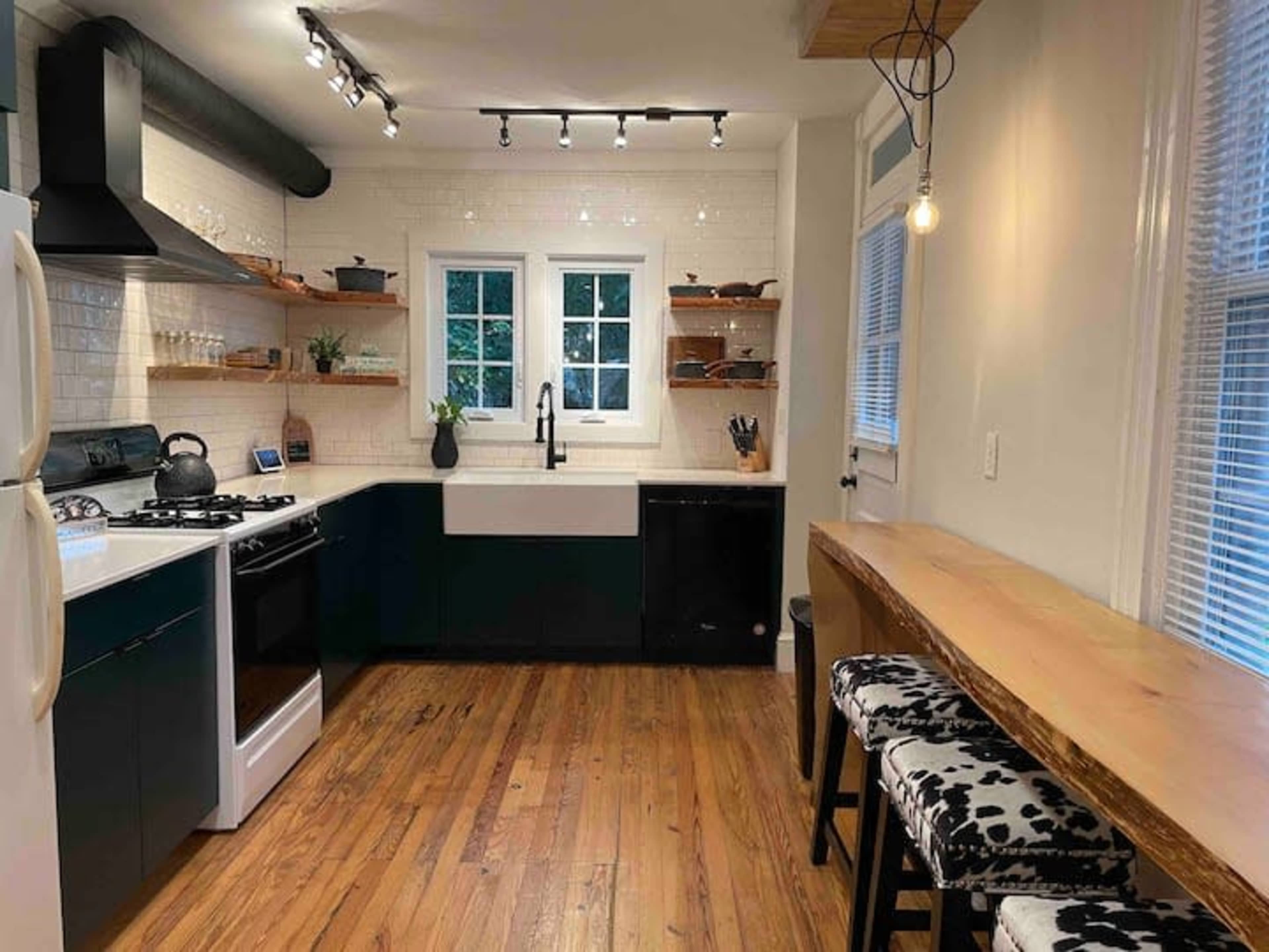 A modern kitchen featuring a black and white color scheme, with wooden shelves, a farmhouse sink, and a small dining area with bar stools.