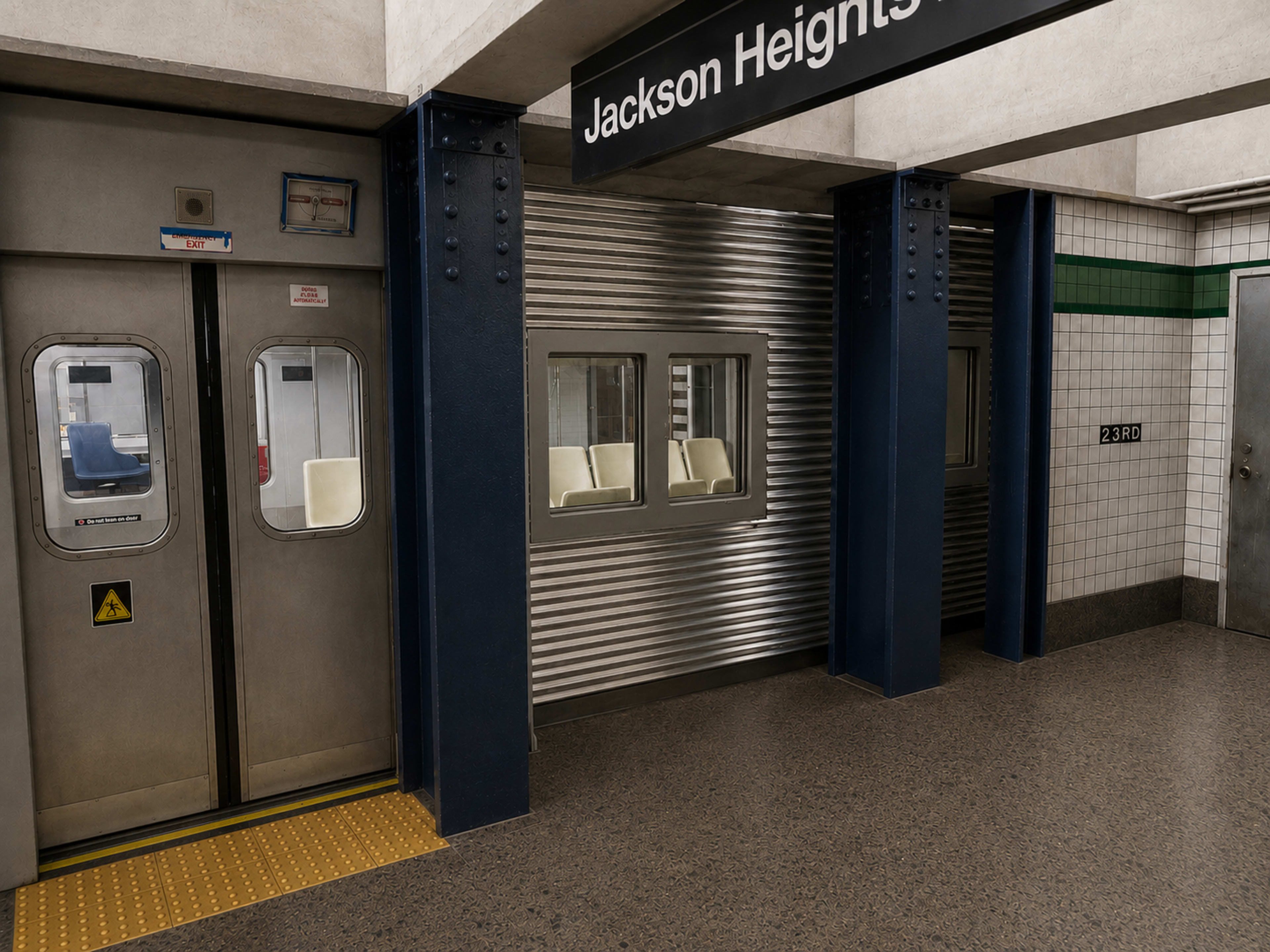 The image shows a subway station platform with a sign displaying "Jackson Heights," featuring metallic sliding doors and a tiled wall.