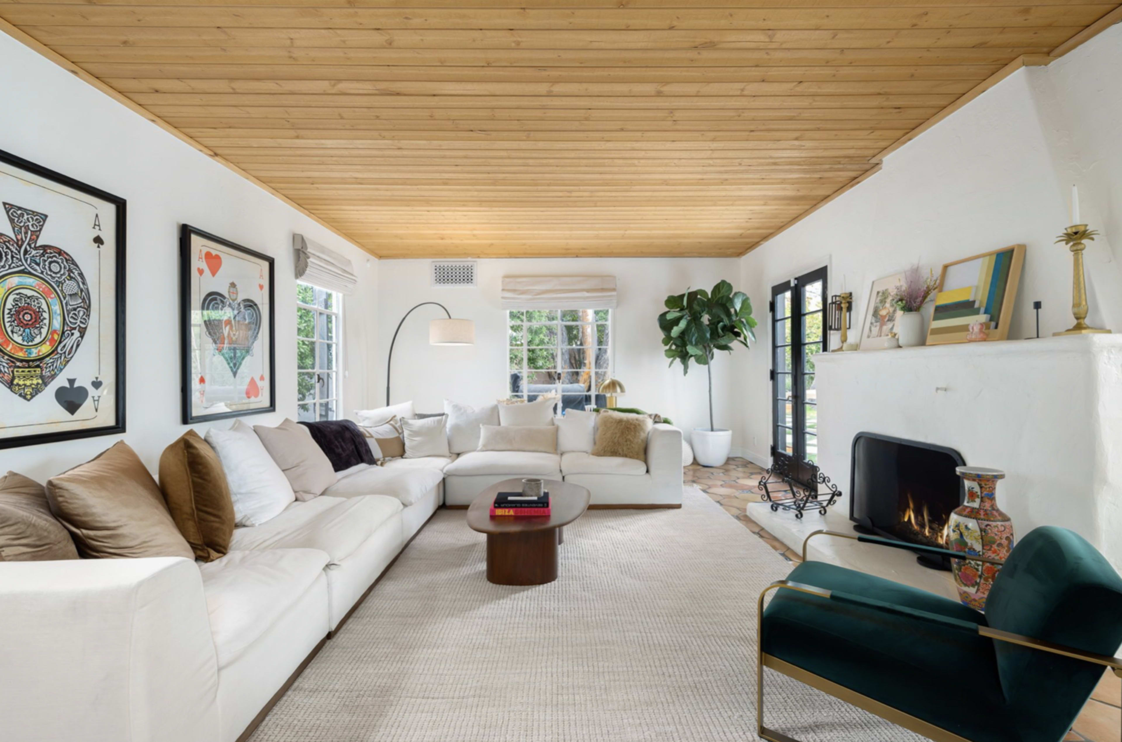 A bright living room features a white sectional sofa, a wooden ceiling, and a cozy fireplace surrounded by decorative art and plants.