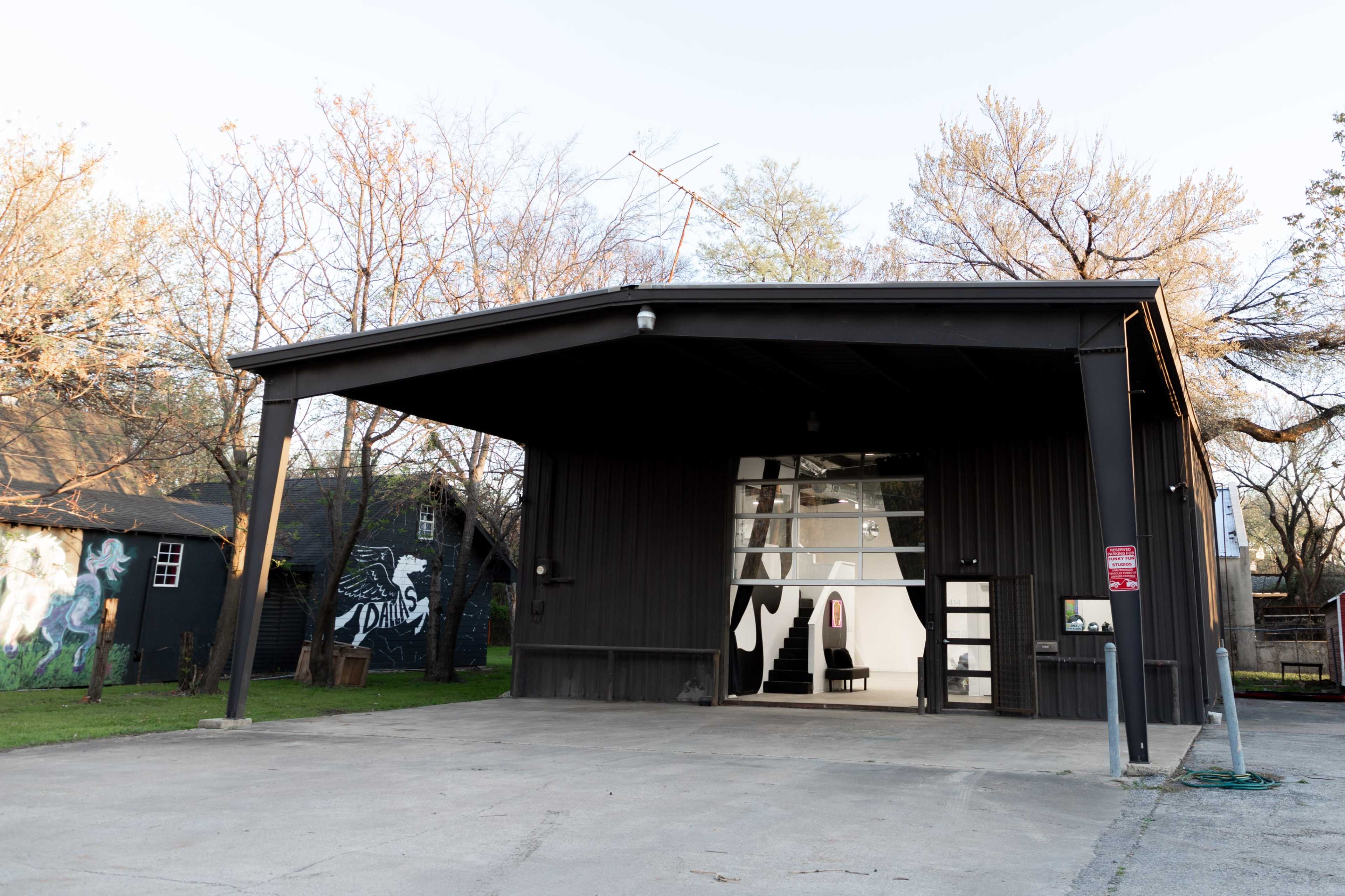 A black metal building with a large front porch and large windows sits on a paved lot, surrounded by bare trees and grassy areas.