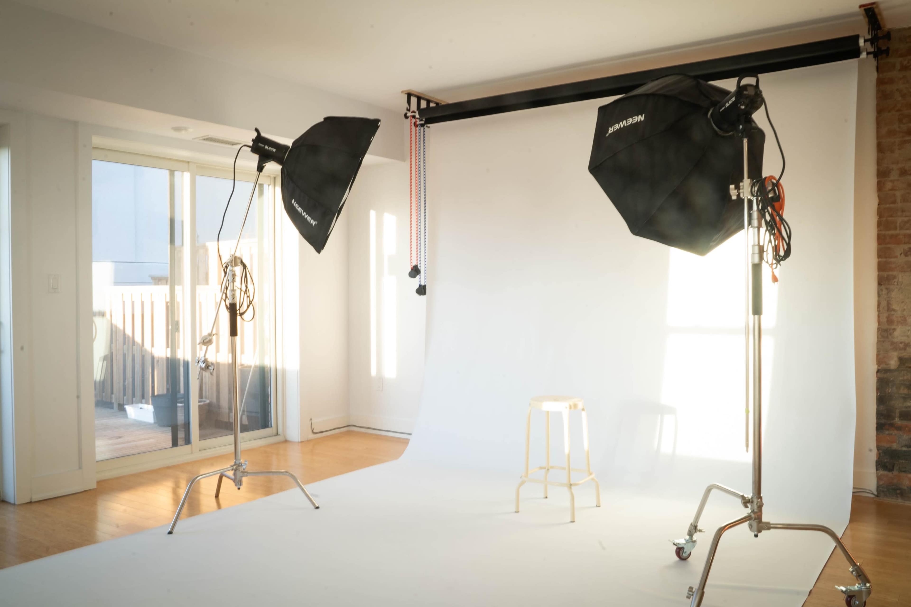 A photography studio setup with two softbox lights and a stool in front of a white backdrop.