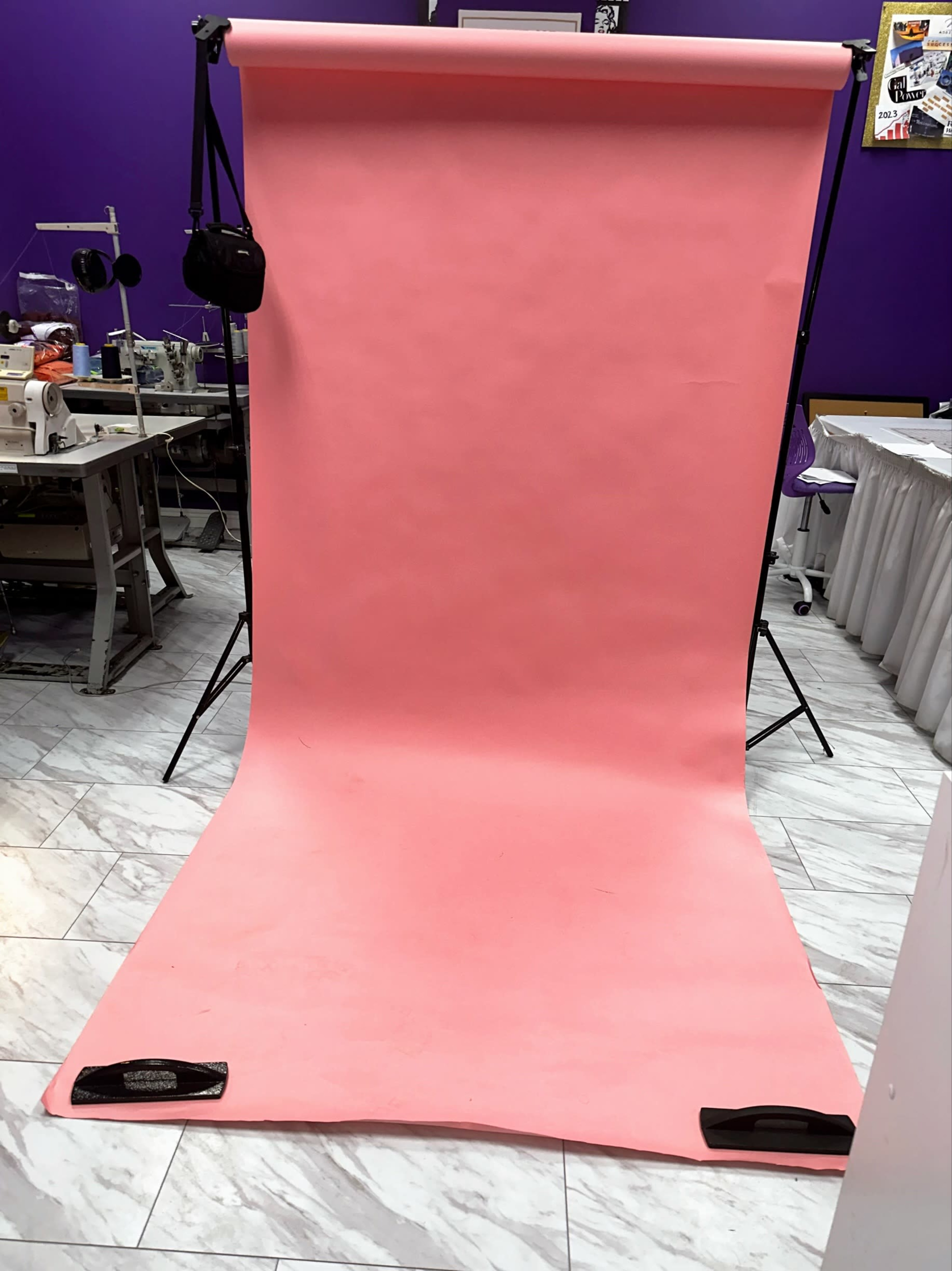 A pink backdrop set up on a stand with a wooden floor beneath it in a studio environment.