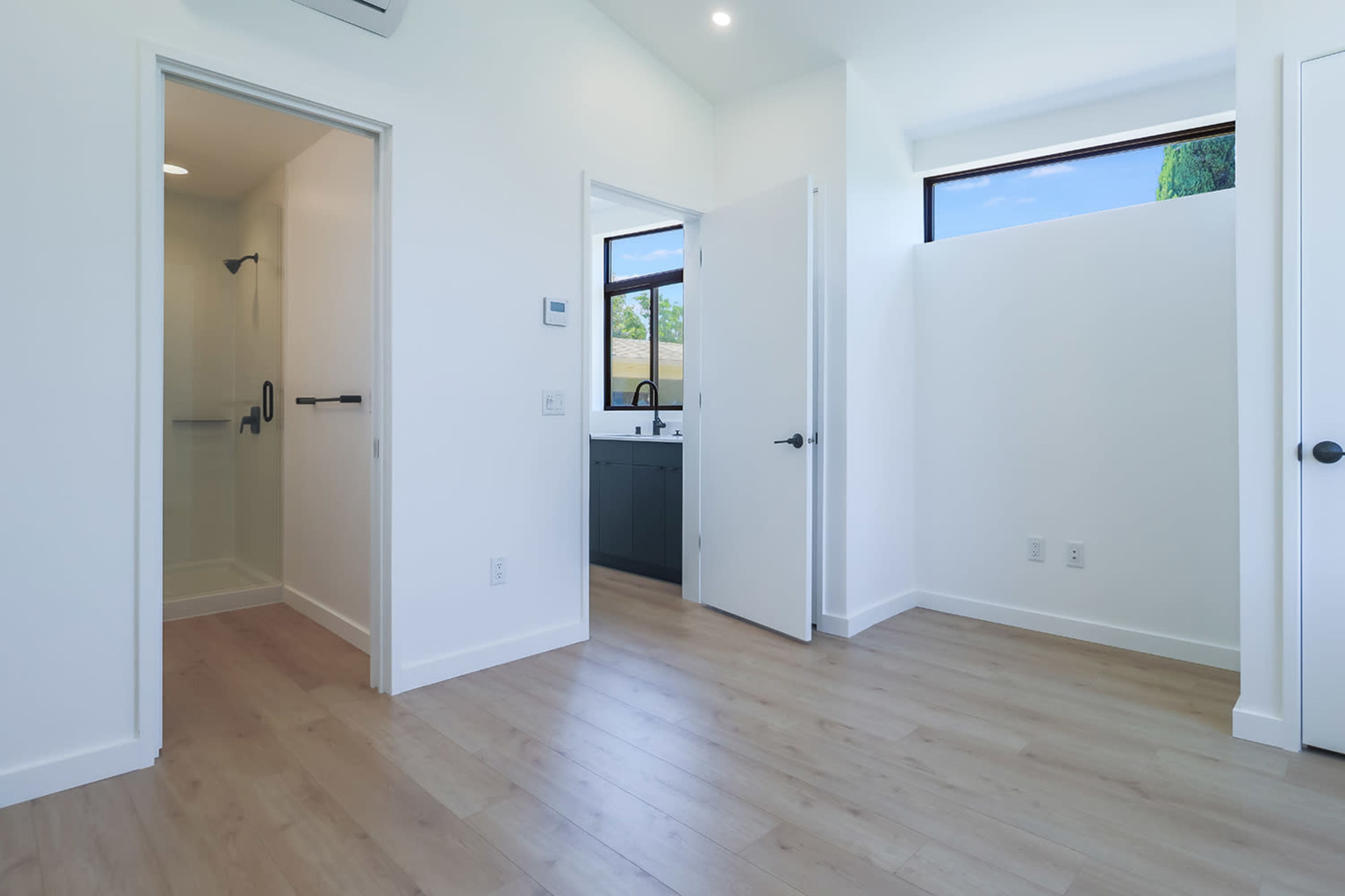A modern interior space with an ensuite bathroom and a room featuring light wood flooring, white walls, and large windows.