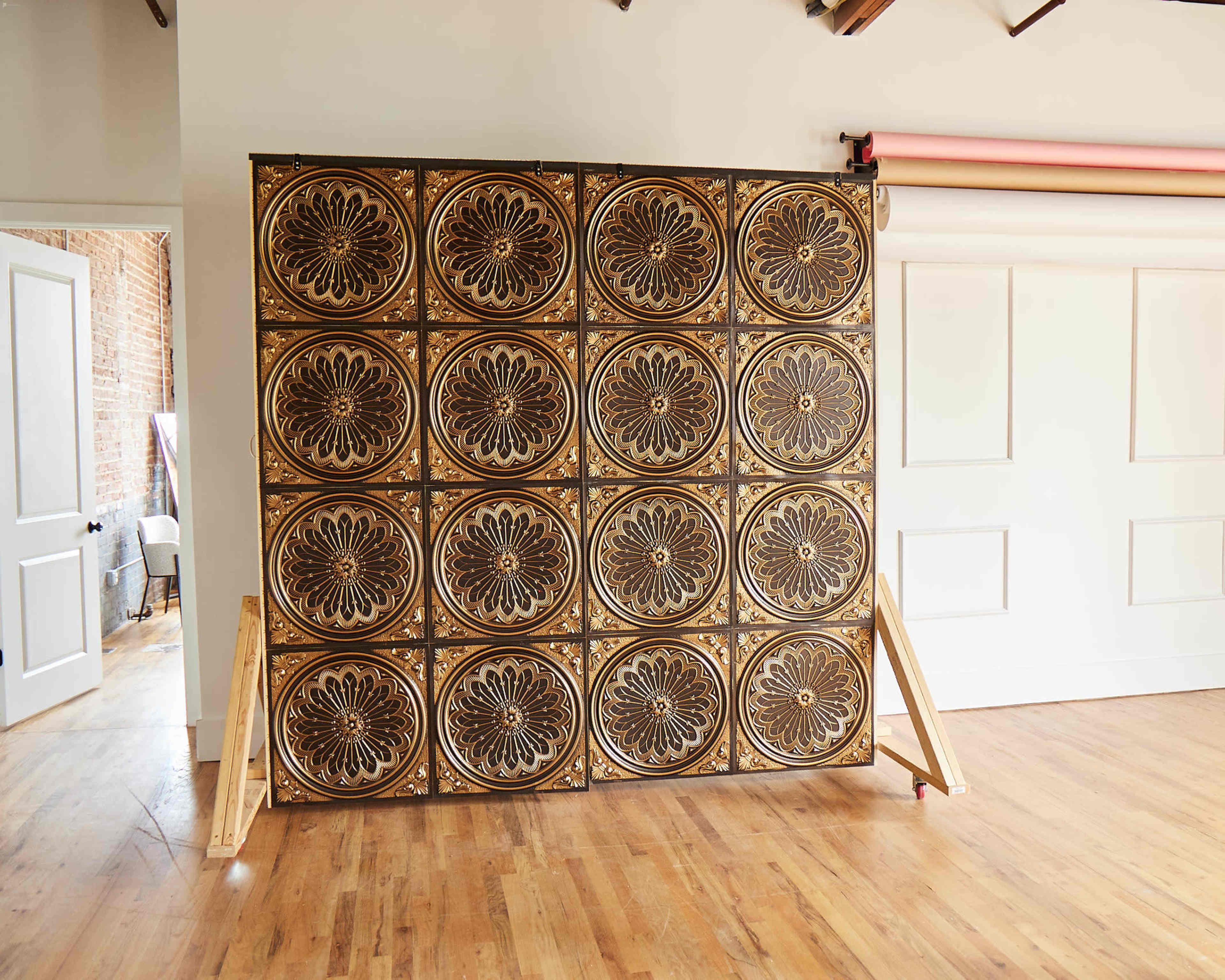 A large decorative wall panel composed of arranged, patterned tiles in a room with wooden flooring.