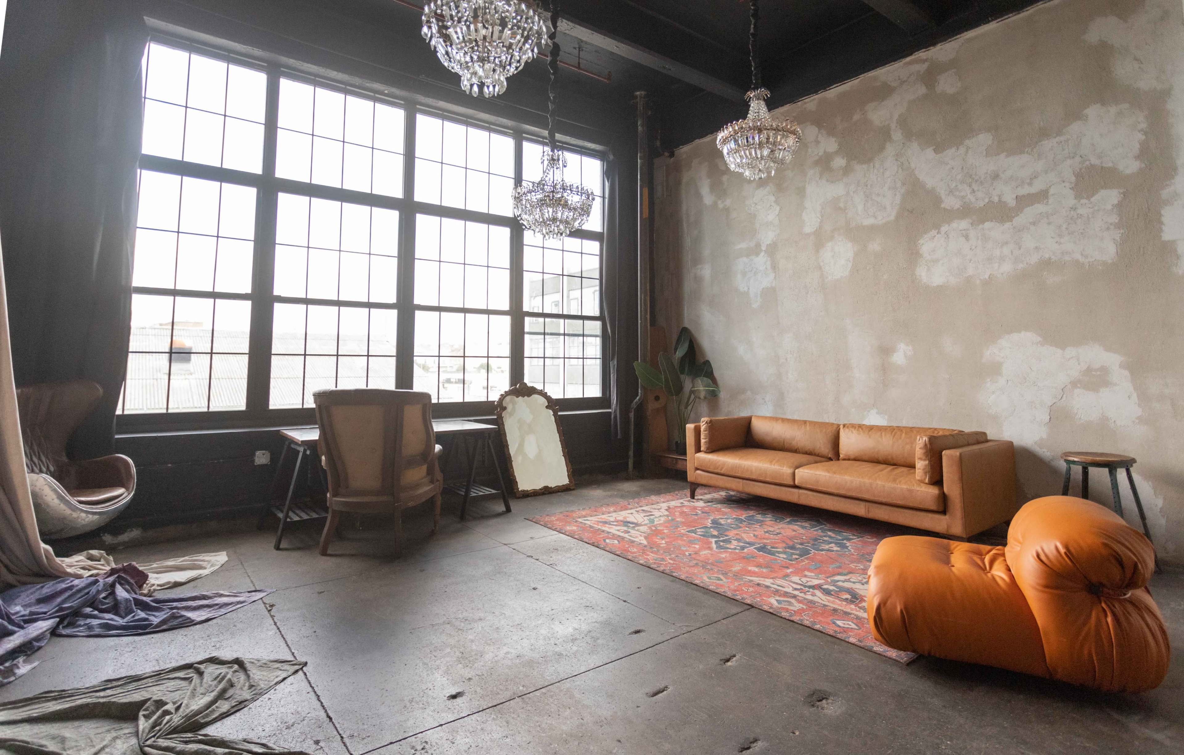 A spacious room with large windows, a sofa, a rug, and various pieces of furniture including a chair and a mirror.