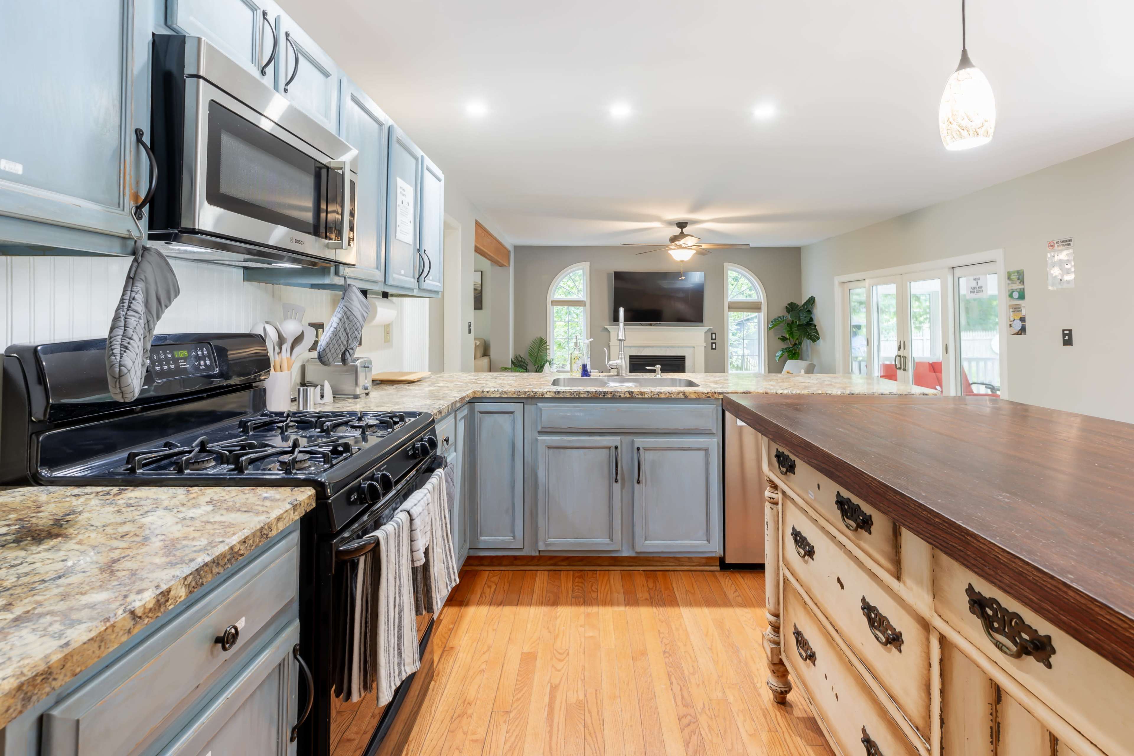 A modern kitchen featuring a blend of blue cabinets and a wooden island with a countertop, equipped with stainless steel appliances and an open layout leading to a living area.