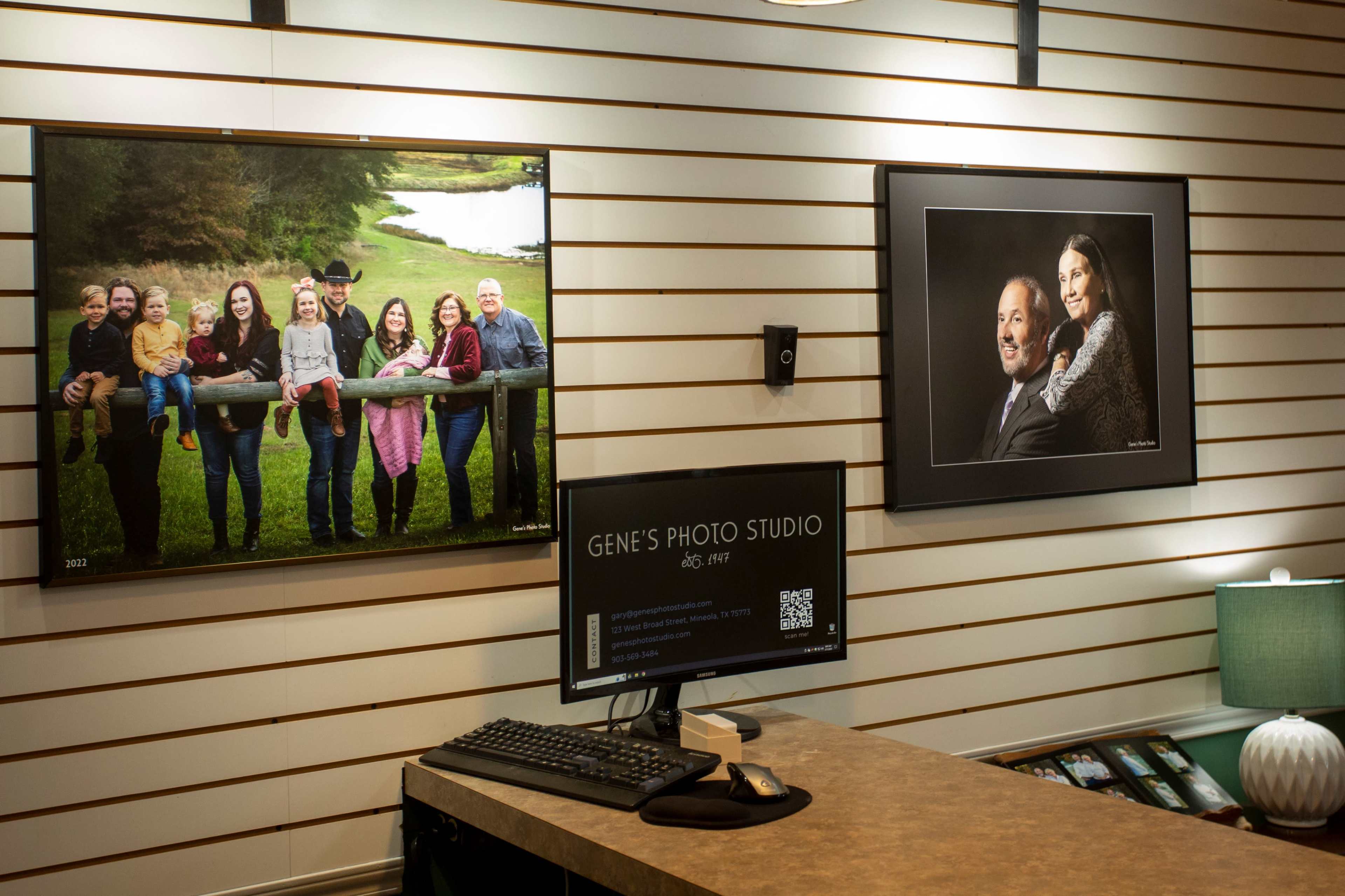 The interior of a photo studio with framed family portraits on the wall and a computer station on a counter.