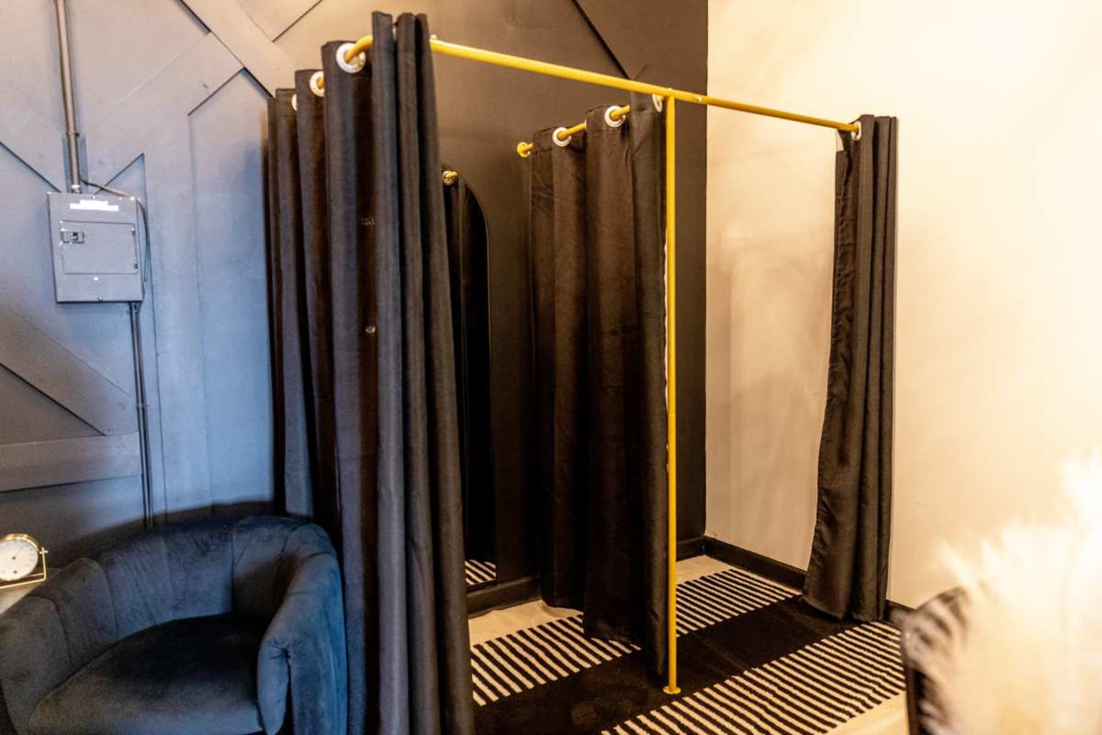 The image shows a clothing fitting area with a yellow rod and black curtains arranged for privacy, situated in a modern room with contrasting flooring.