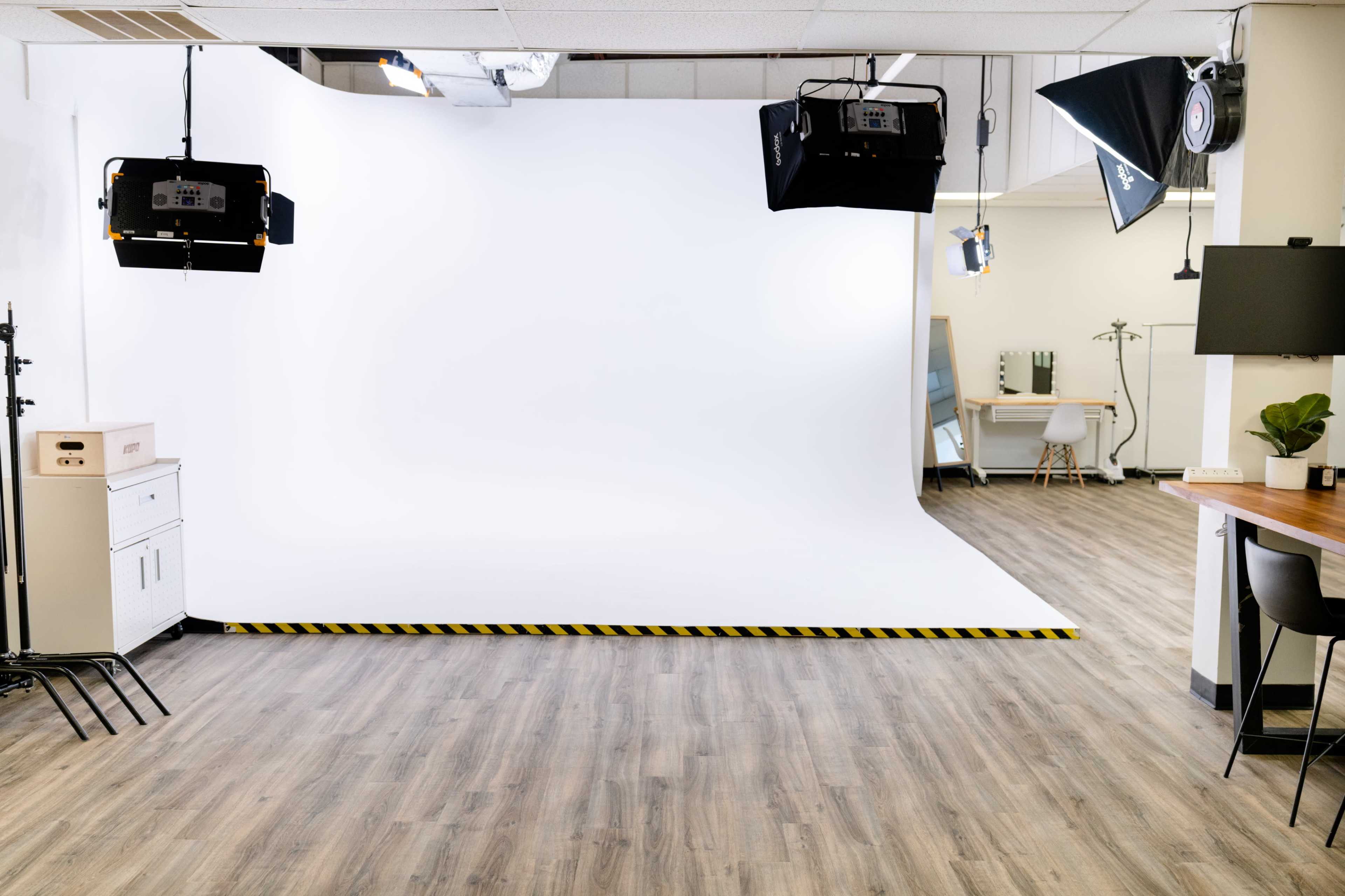 A photography studio with a white backdrop, spotlights, and wooden flooring.