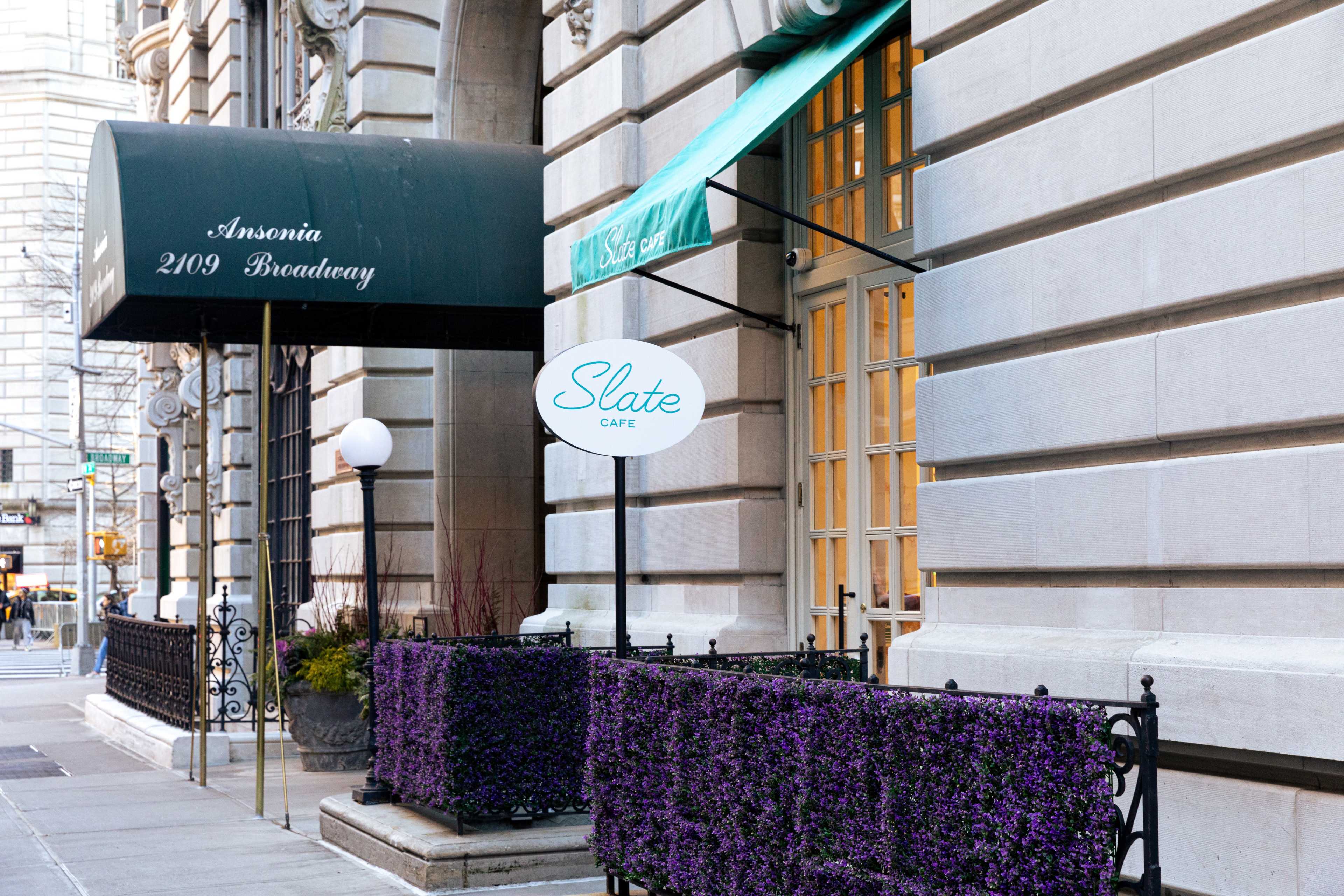 The exterior of a café named "Slate Café" features a sign in front of a building with tall windows and a green awning.