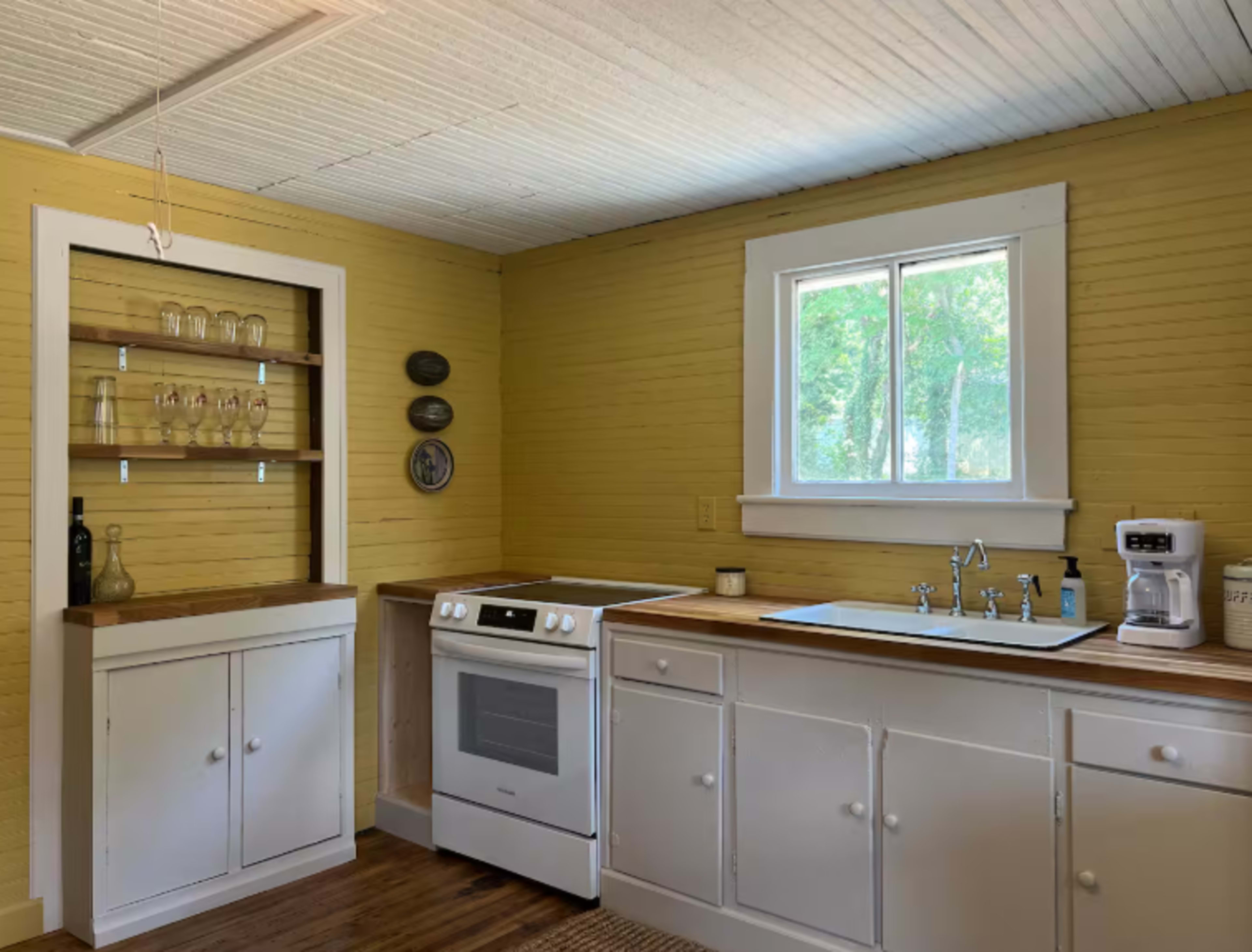 The image shows a kitchen featuring a white stove, a sink with a faucet, wooden countertops, and yellow-painted walls.