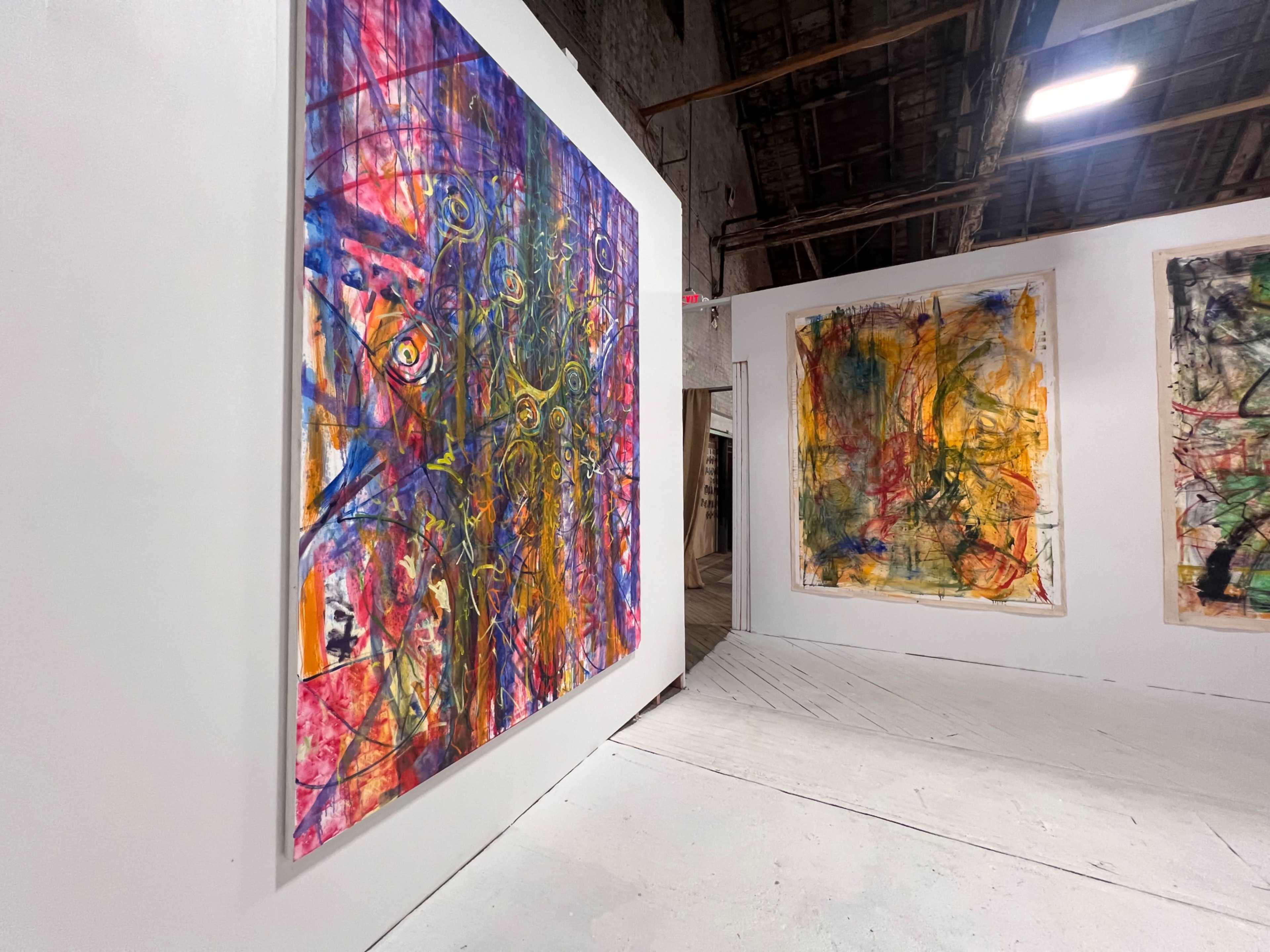 The image shows an art gallery with large, colorful abstract paintings displayed on white walls and a spacious, well-lit interior.