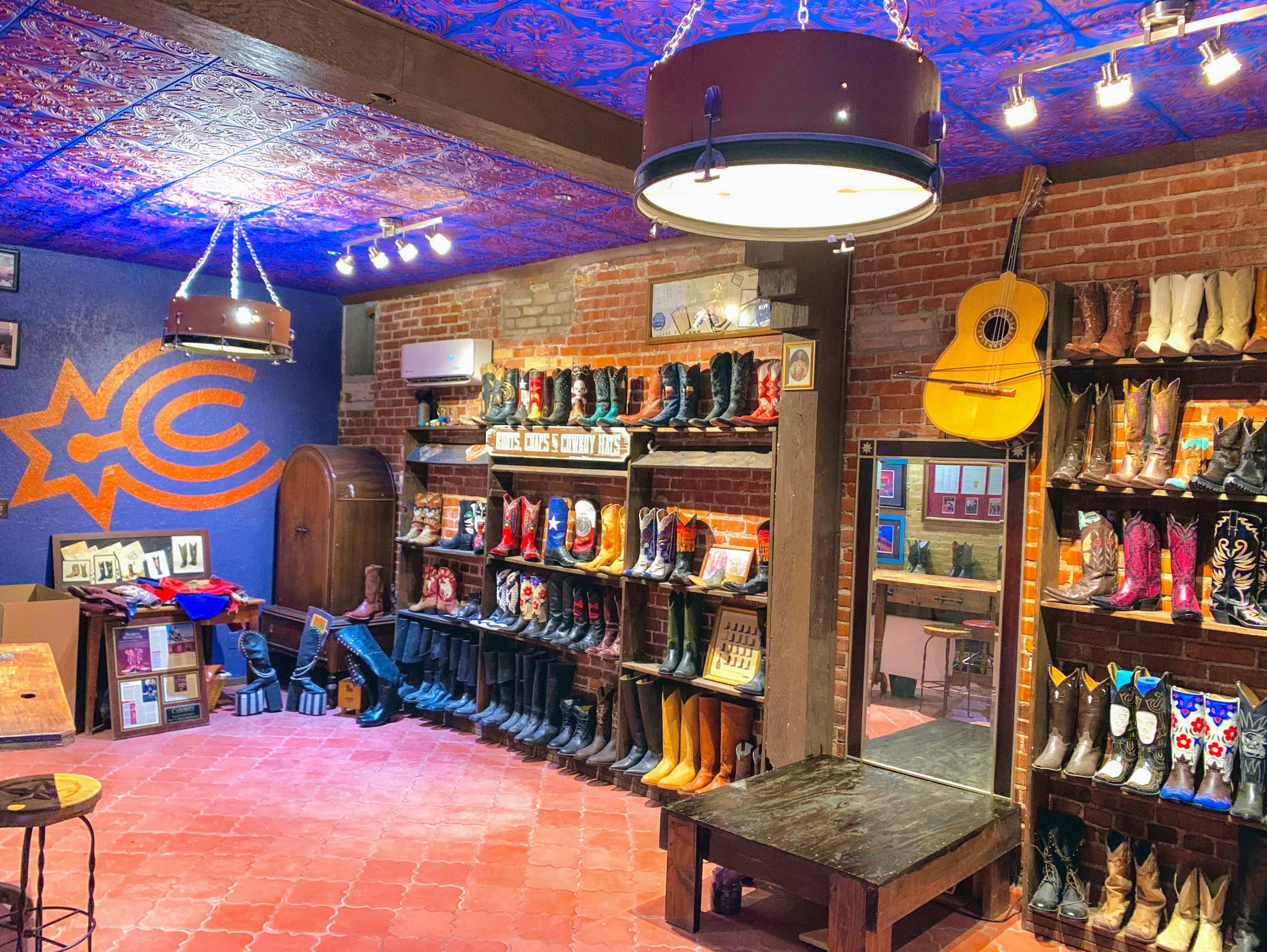 A cozy shop features wooden shelves filled with various styles of cowboy boots, accented by a colorful ceiling and decorated walls.