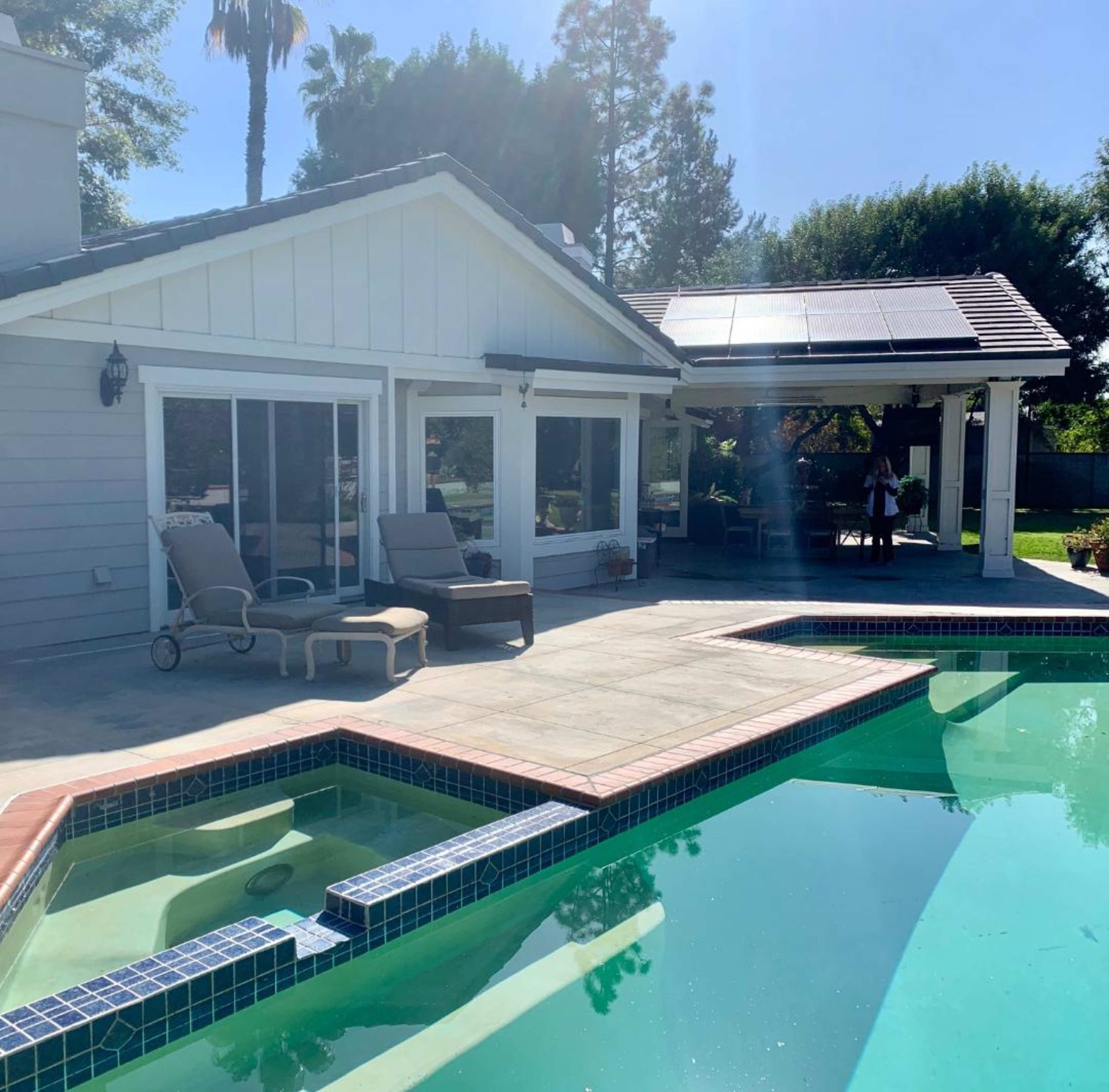 A modern house with a pool and patio area, featuring a solar panel on the roof and loungers beside the water.