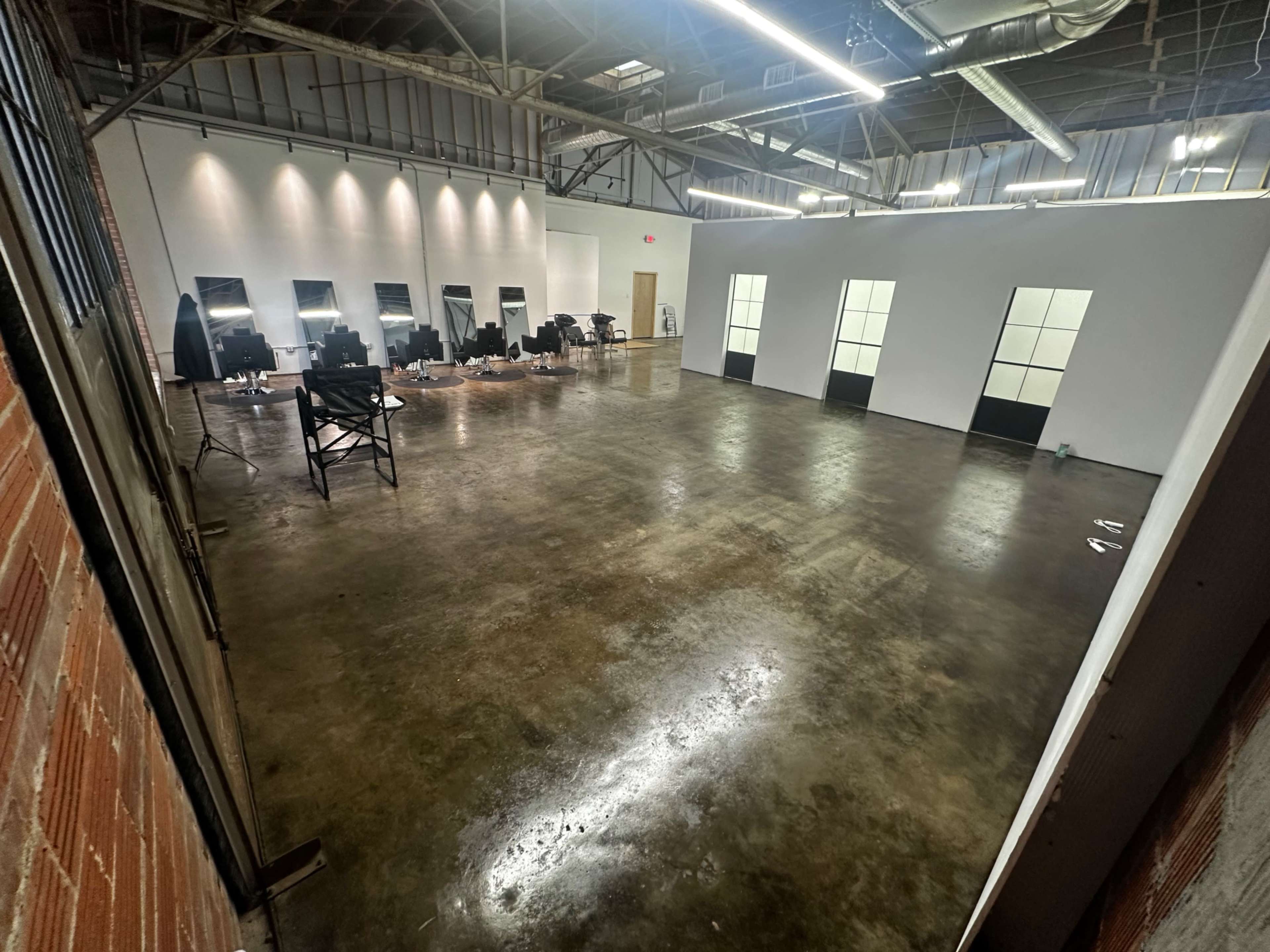 An empty room with polished concrete floors, several empty chairs, and illuminated mirrors along one wall.