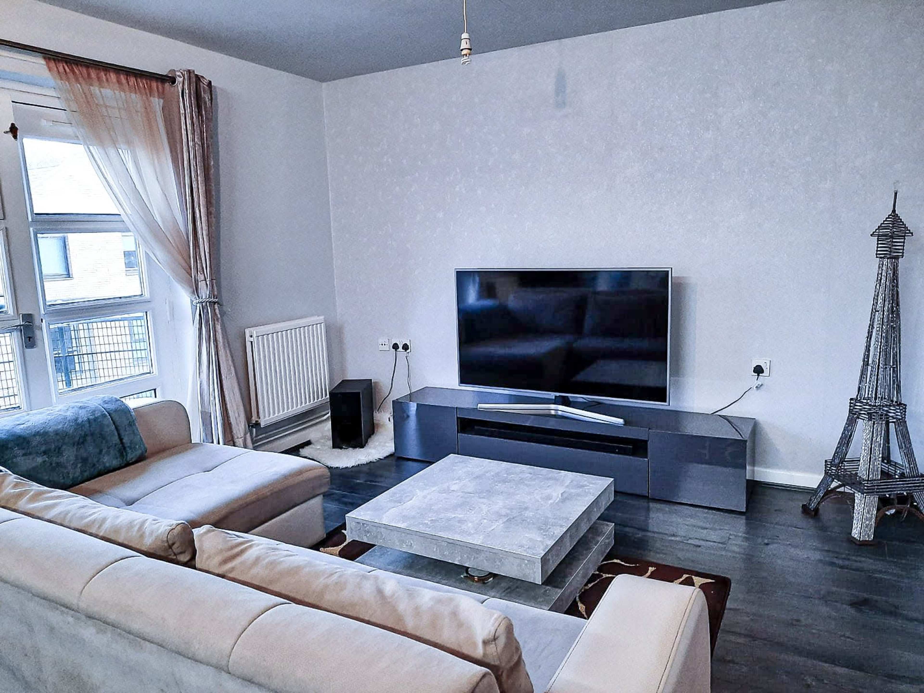 A modern living room featuring a sectional sofa, a coffee table, a large television mounted on a wall unit, and a decorative Eiffel Tower figurine.