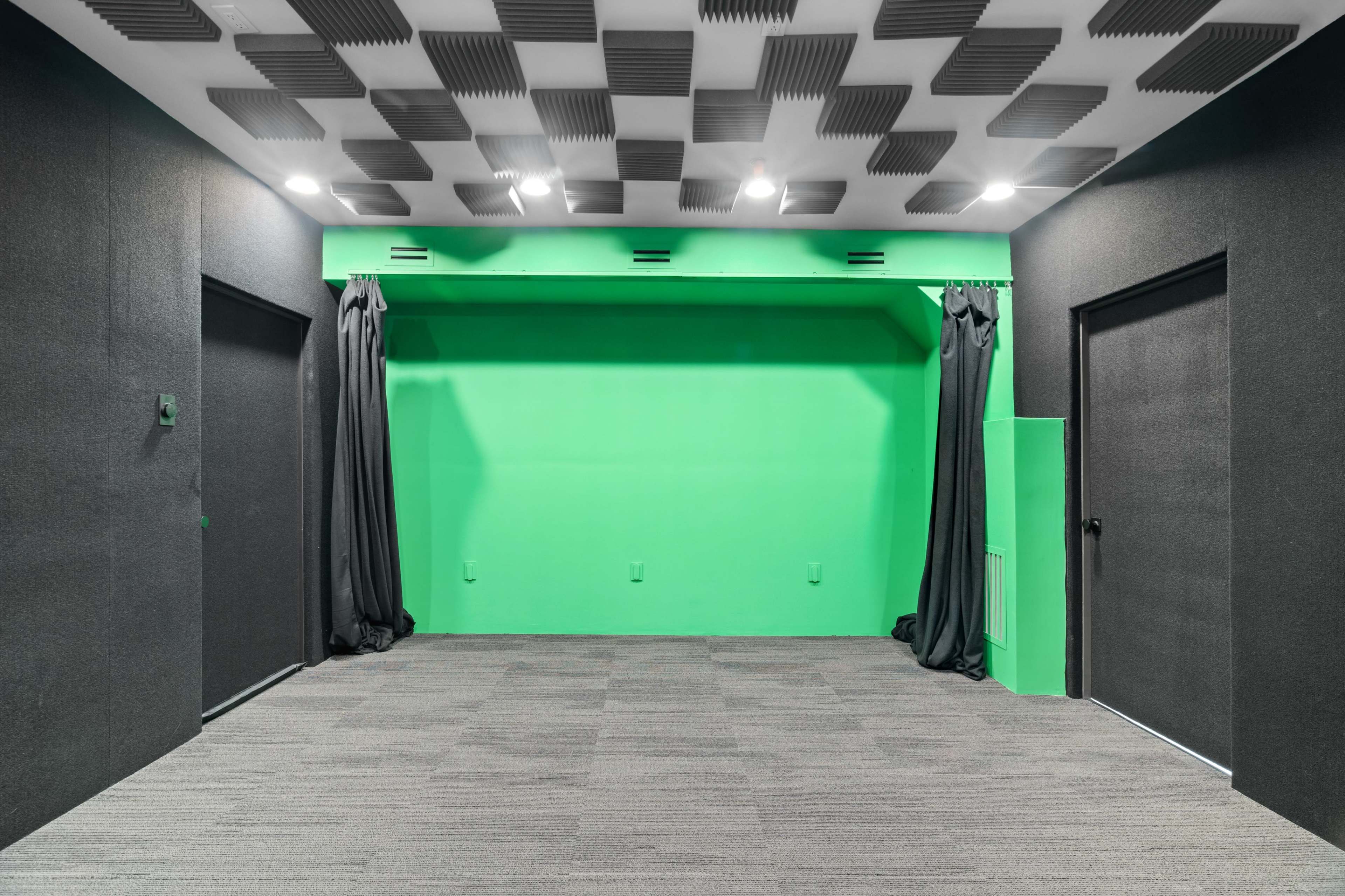 A soundproofed room with a green screen backdrop, two dark doors, and a carpeted floor.