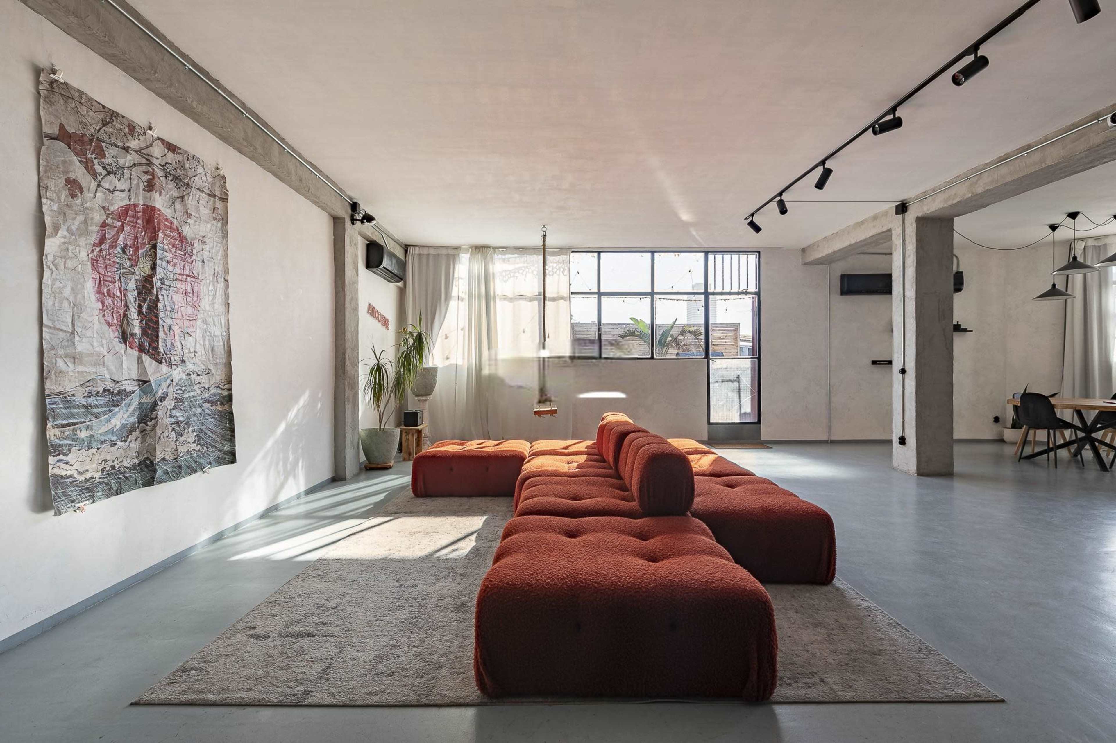 The image shows a spacious, modern living area with an orange modular sofa, a large window, and minimalist decor.