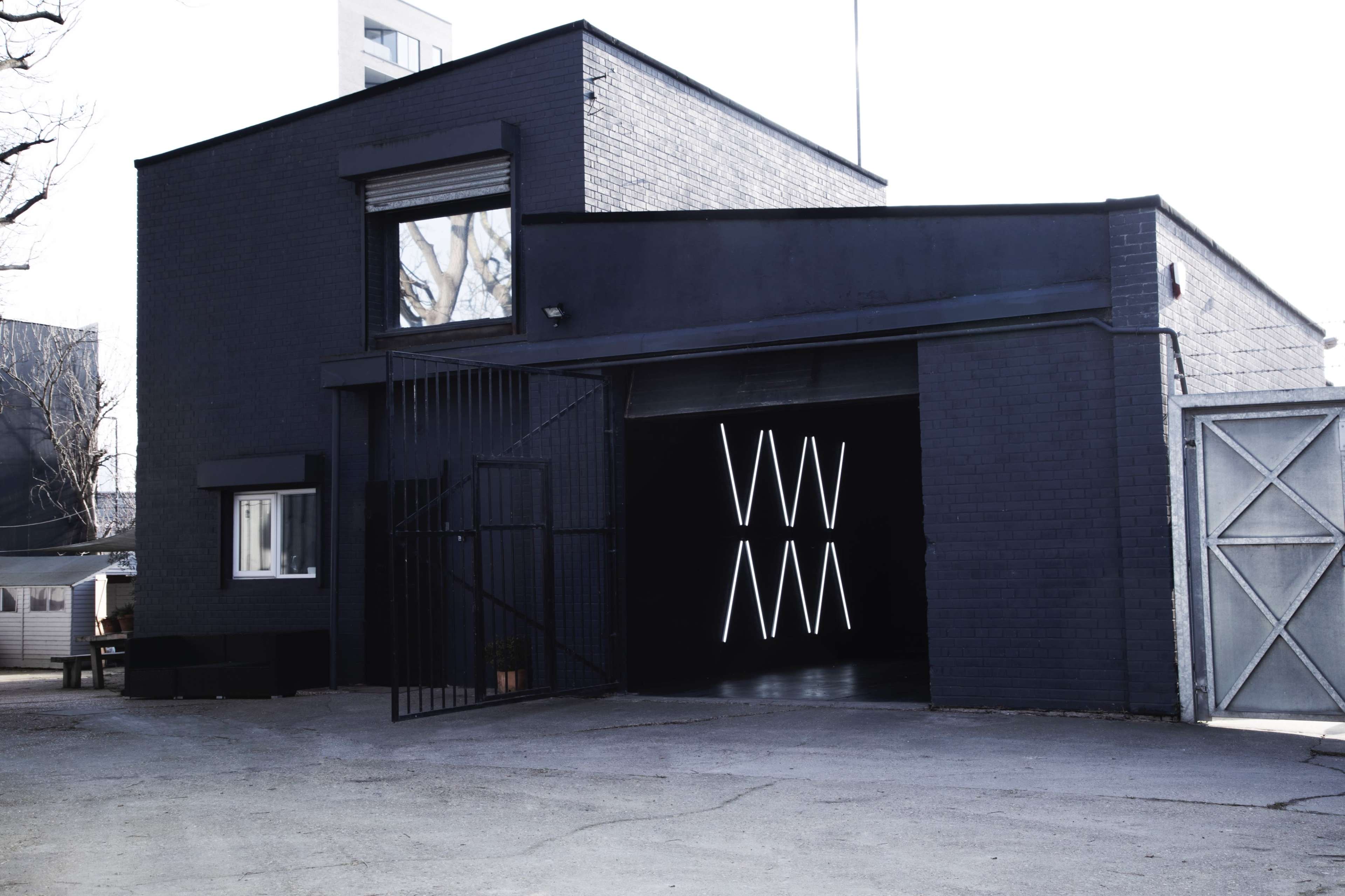 A black building features an open garage door with illuminated neon lines visible inside.