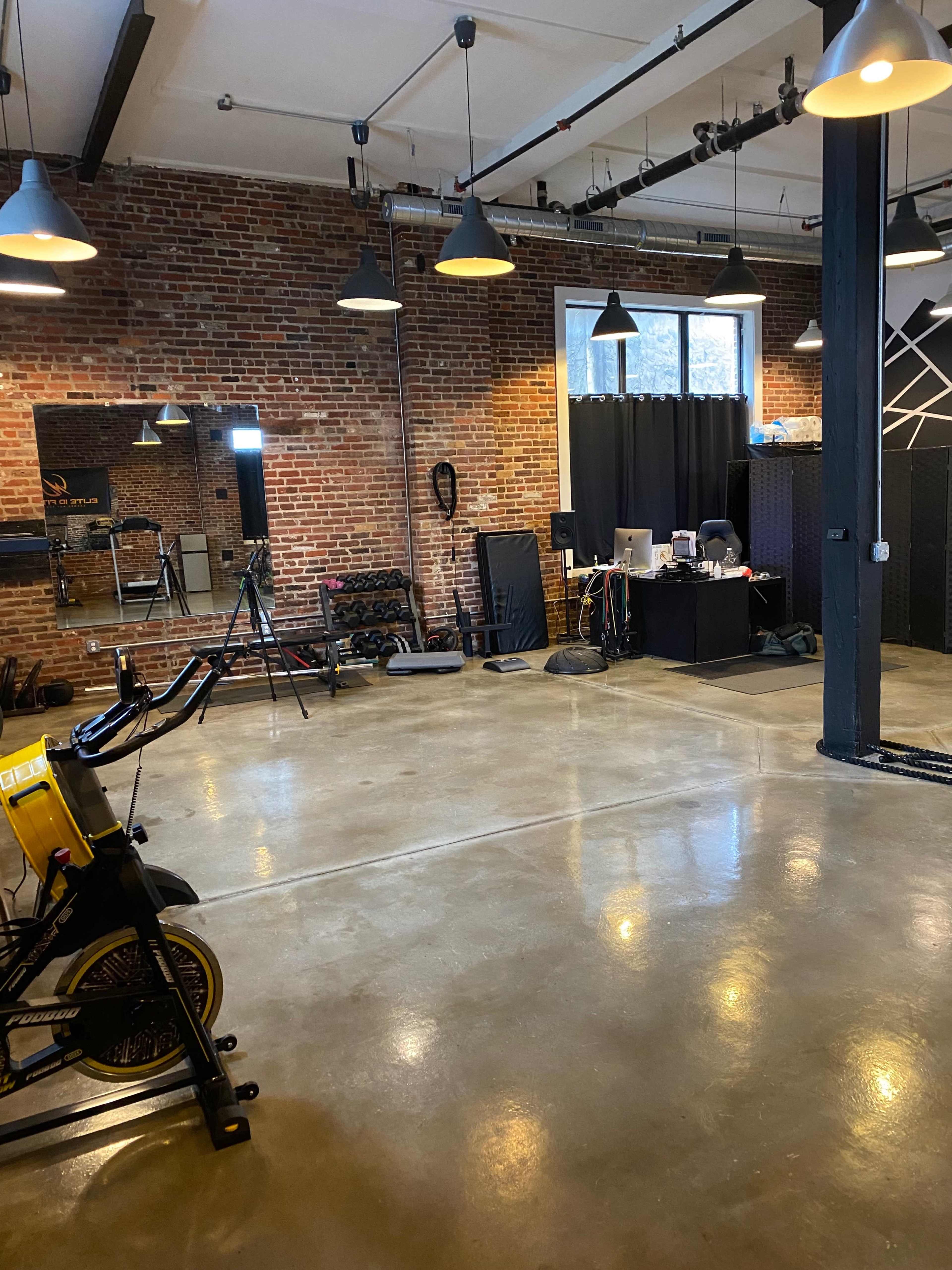 A spacious gym with brick walls, exercise equipment, and a desk area with a computer.