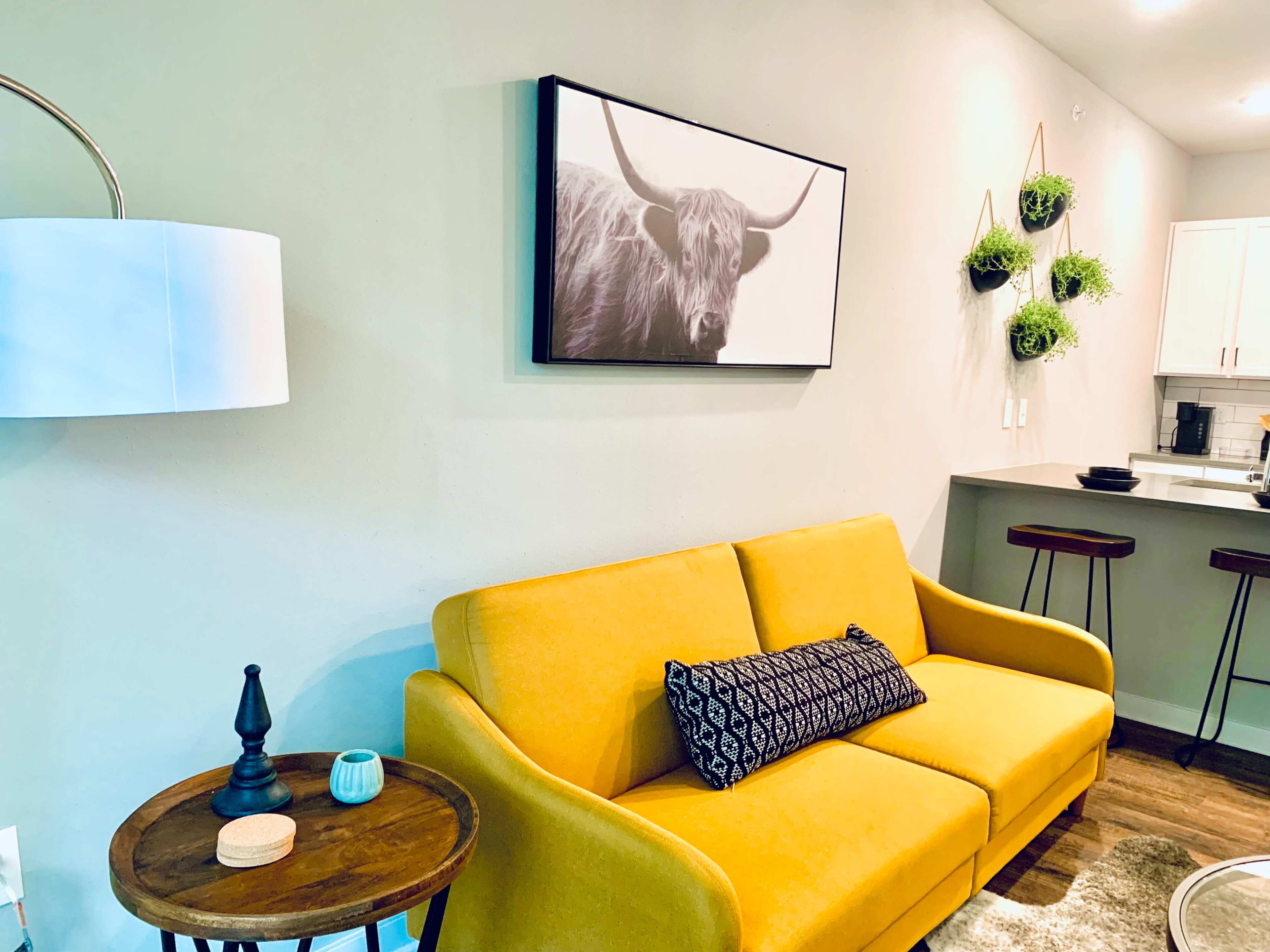 A modern living room with a yellow sofa, a round wooden side table, and a black-and-white bull portrait on the wall.