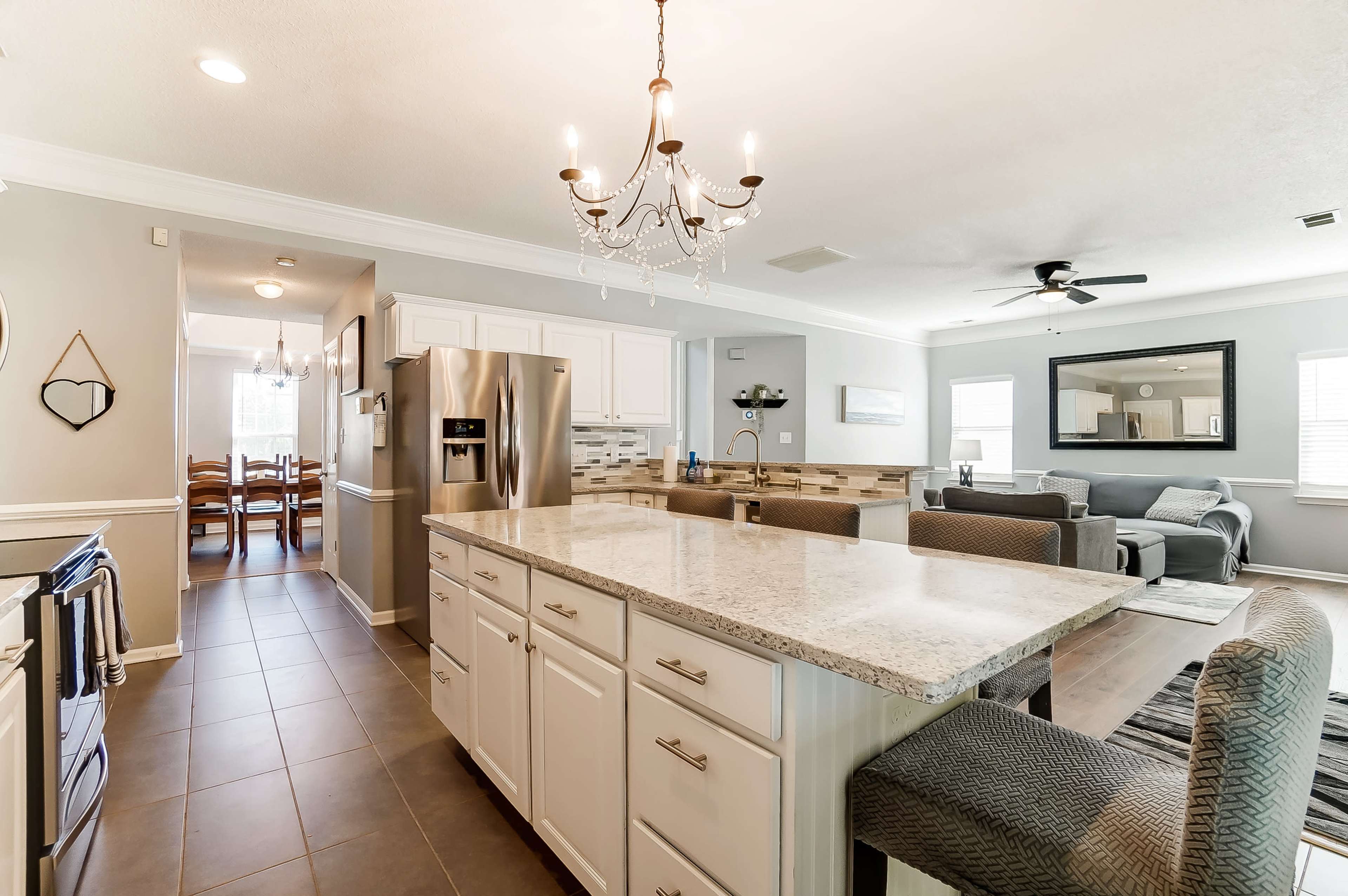 A modern kitchen with white cabinetry, a granite island with seating, and an open layout leading to a living area.