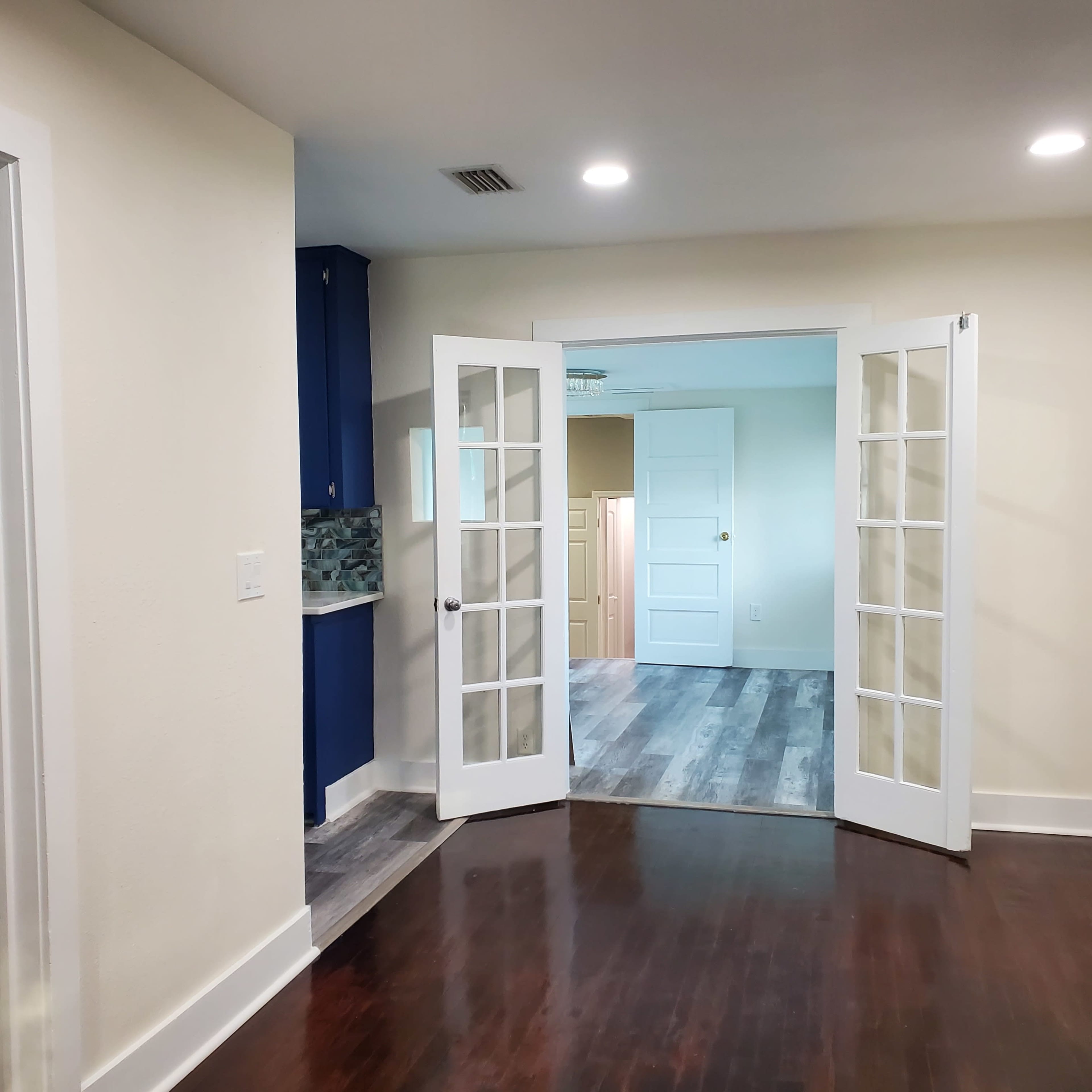 A hallway with open double doors leading into a brightly lit room with pale walls and light-colored flooring.